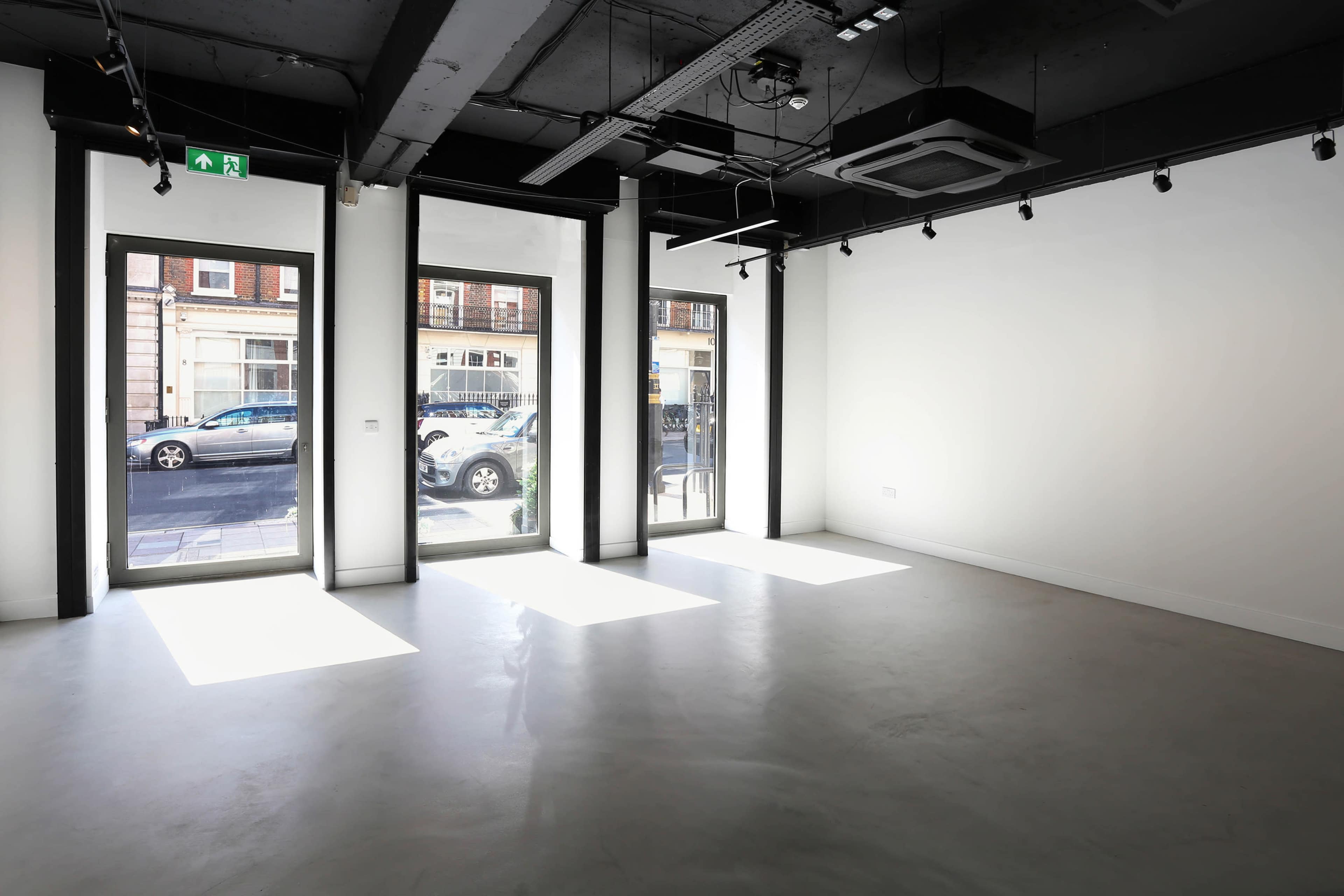 The image shows an empty retail space with concrete flooring and large windows allowing natural light to enter.
