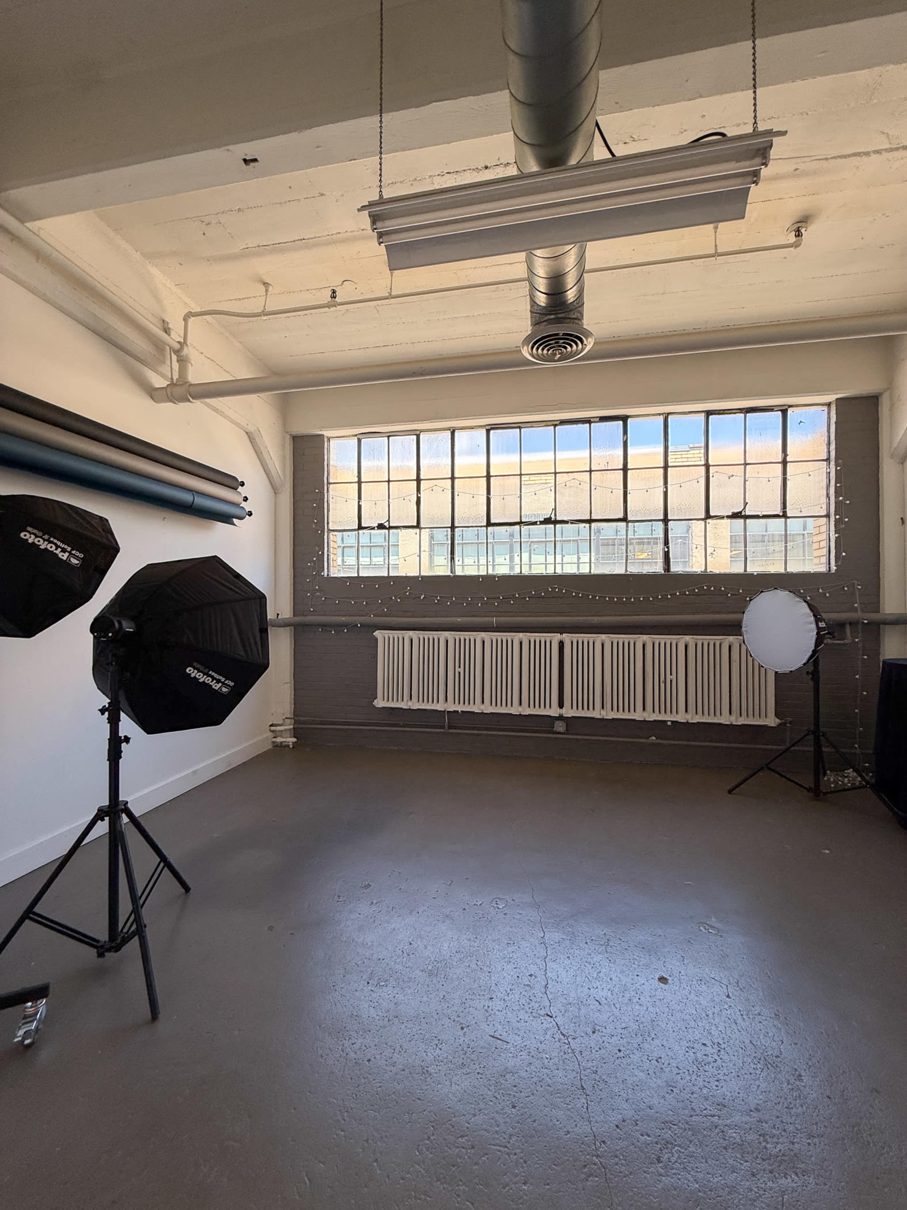 The image shows a spacious photography studio with large windows, softbox lights, and a circular reflector.