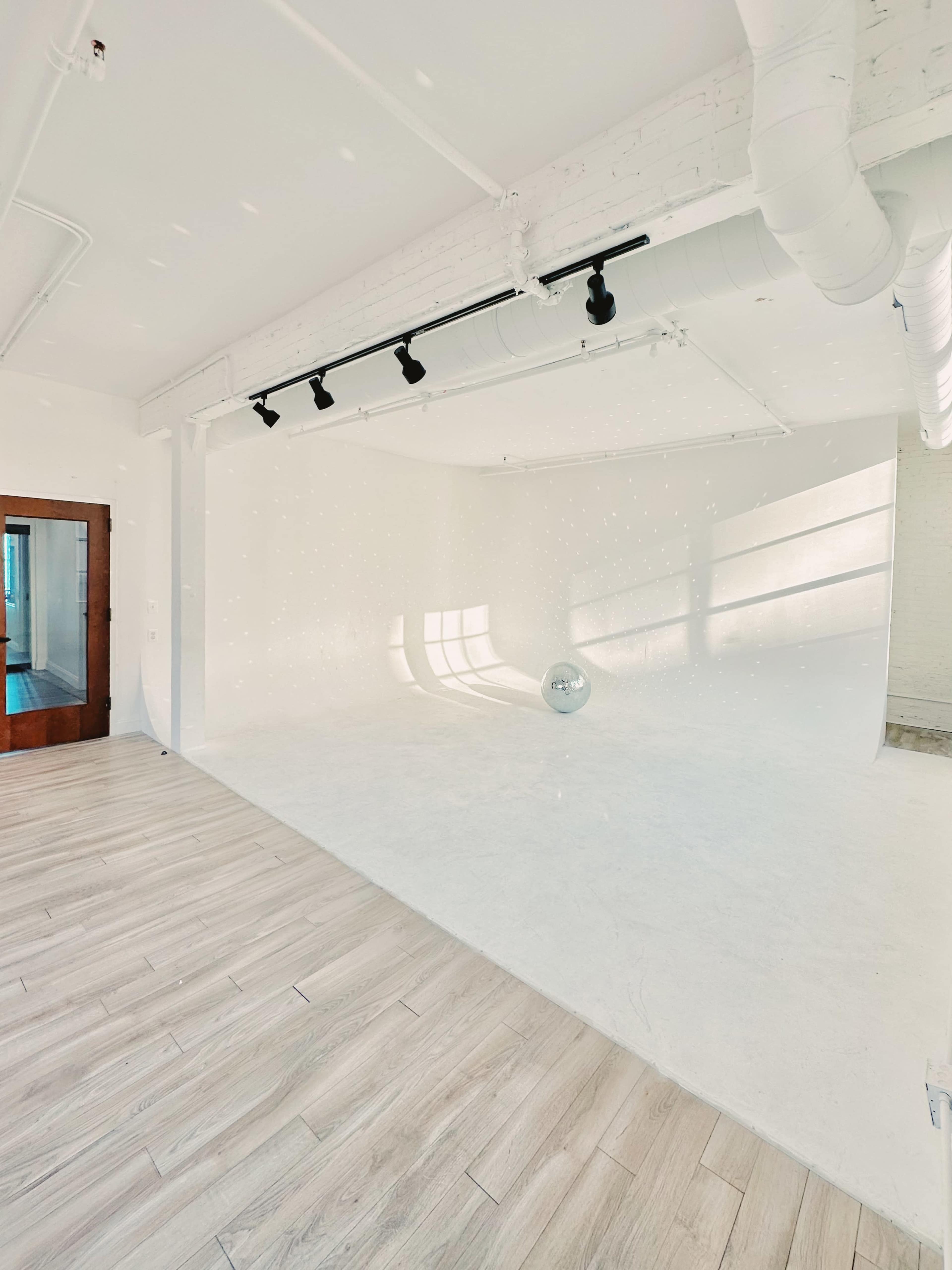 A spacious, well-lit studio with a white backdrop, a disco ball, and wooden flooring.