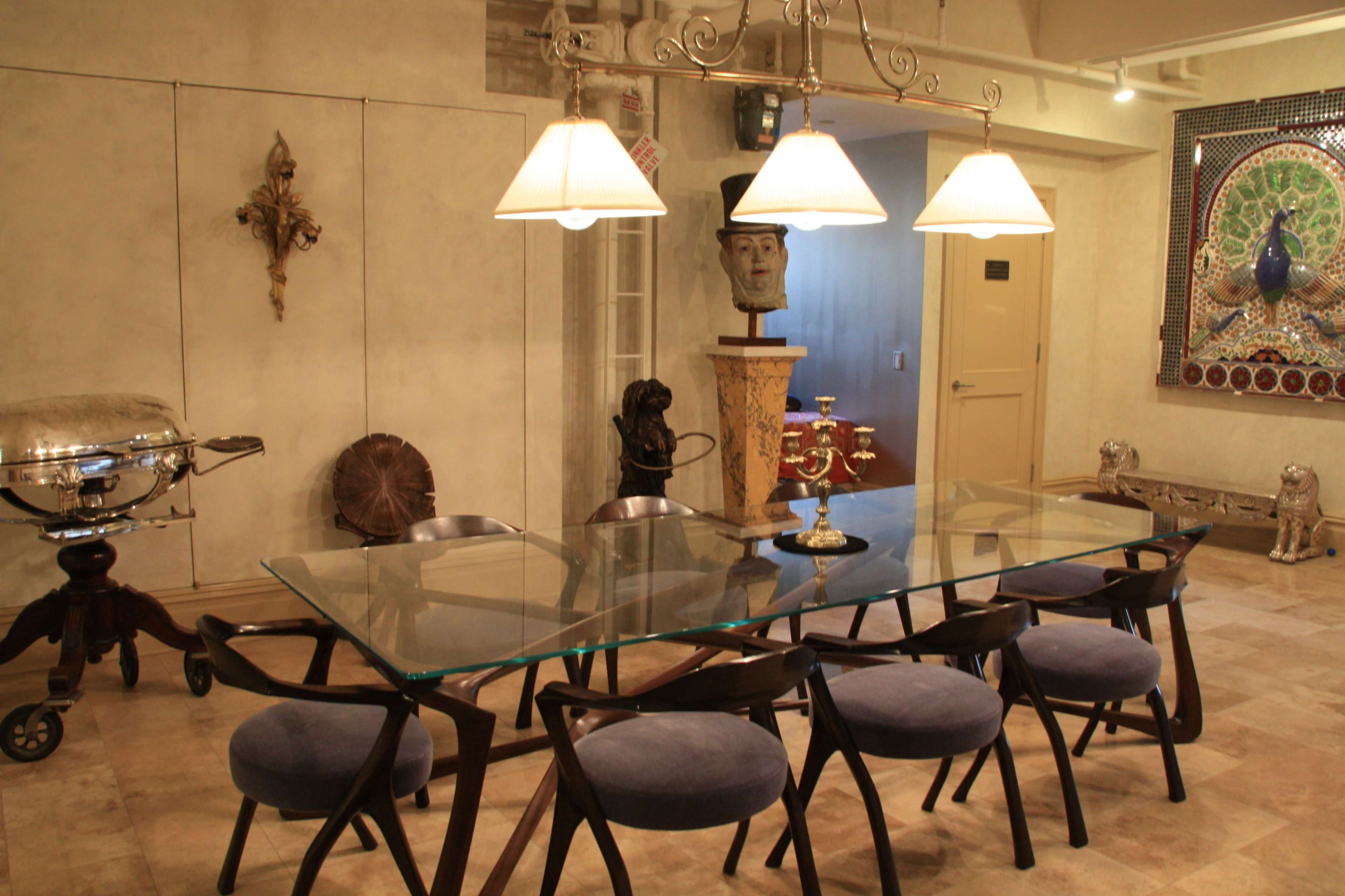 A modern dining room features a large glass table surrounded by eight dark wooden chairs, with a sculpture and decorative wall art in the background.