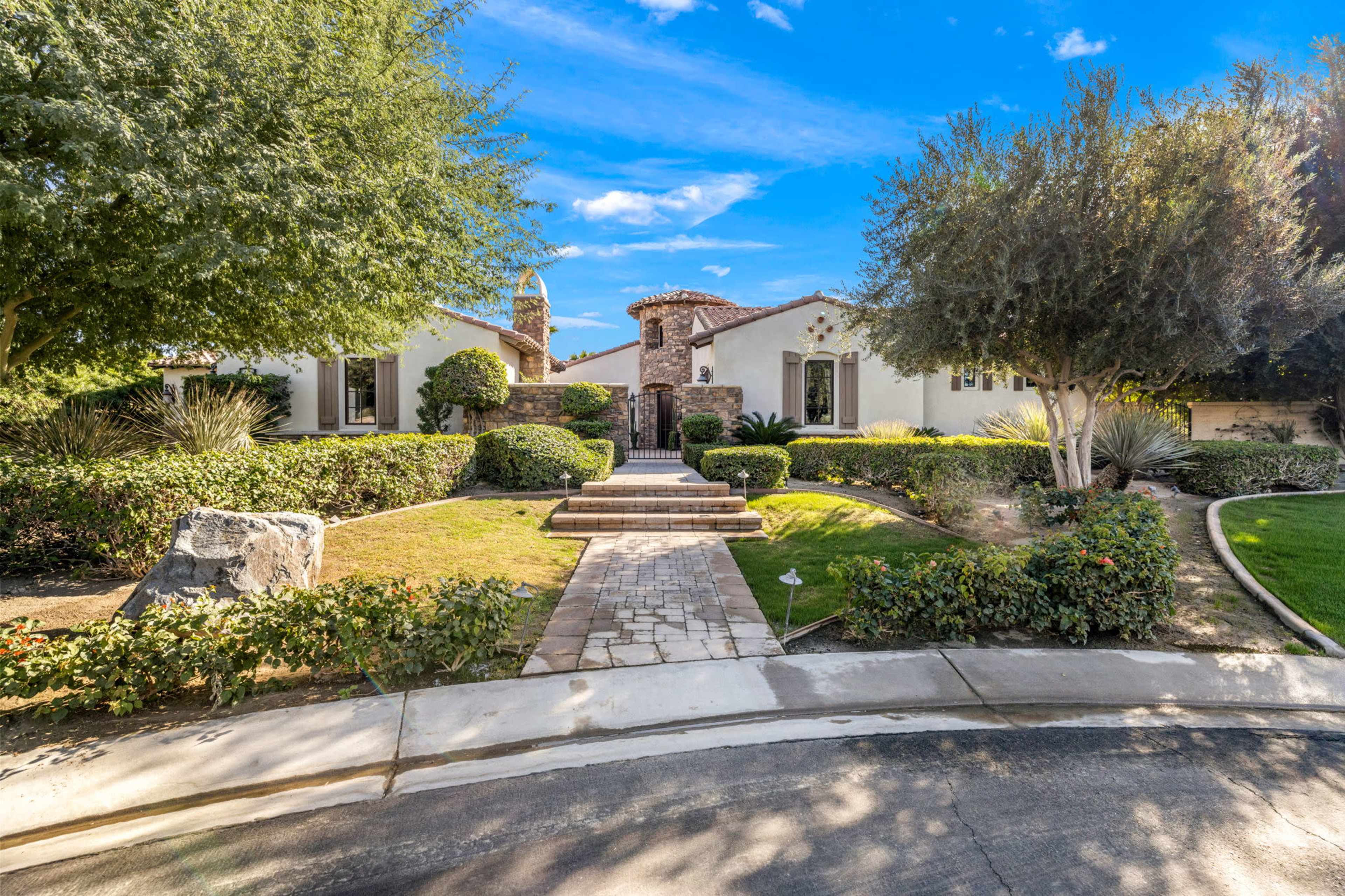 A well-manicured pathway leads to a Mediterranean-style home with lush landscaping and stone accents.
