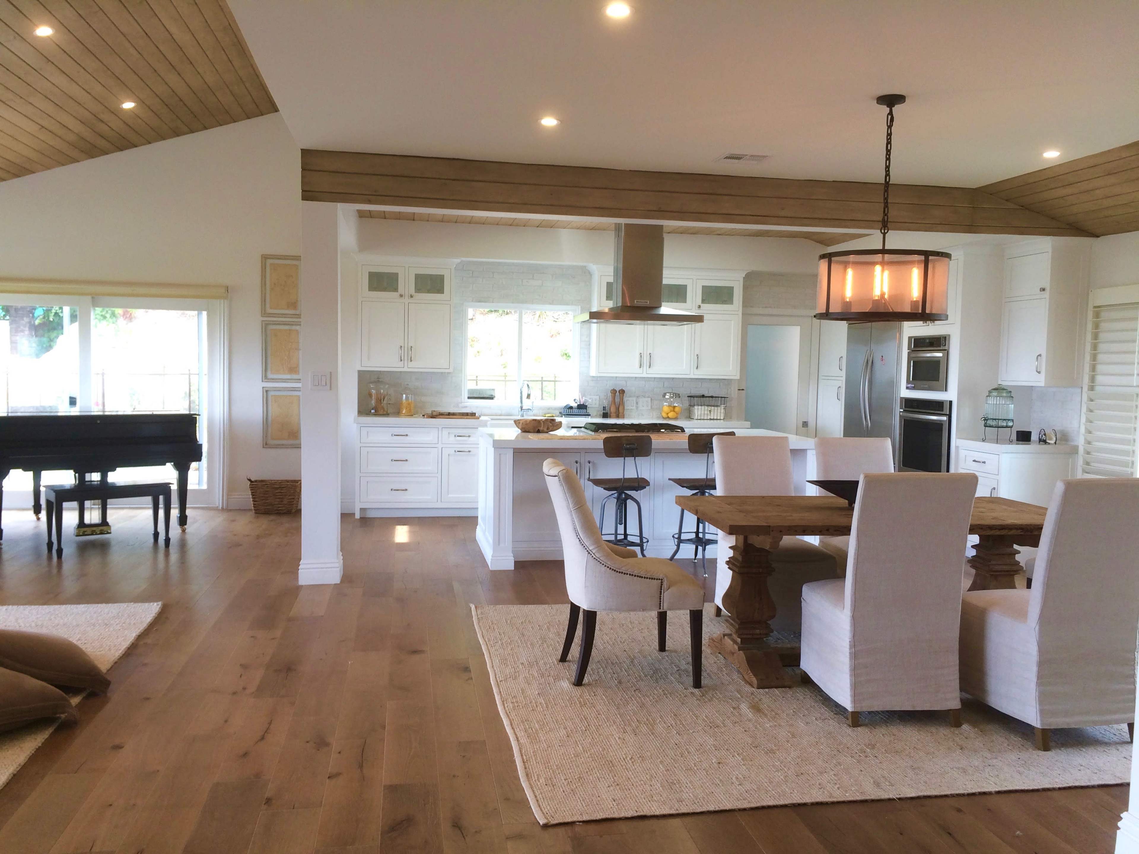 A modern open-concept kitchen and dining area featuring a wooden table surrounded by upholstered chairs, with a piano in the background.