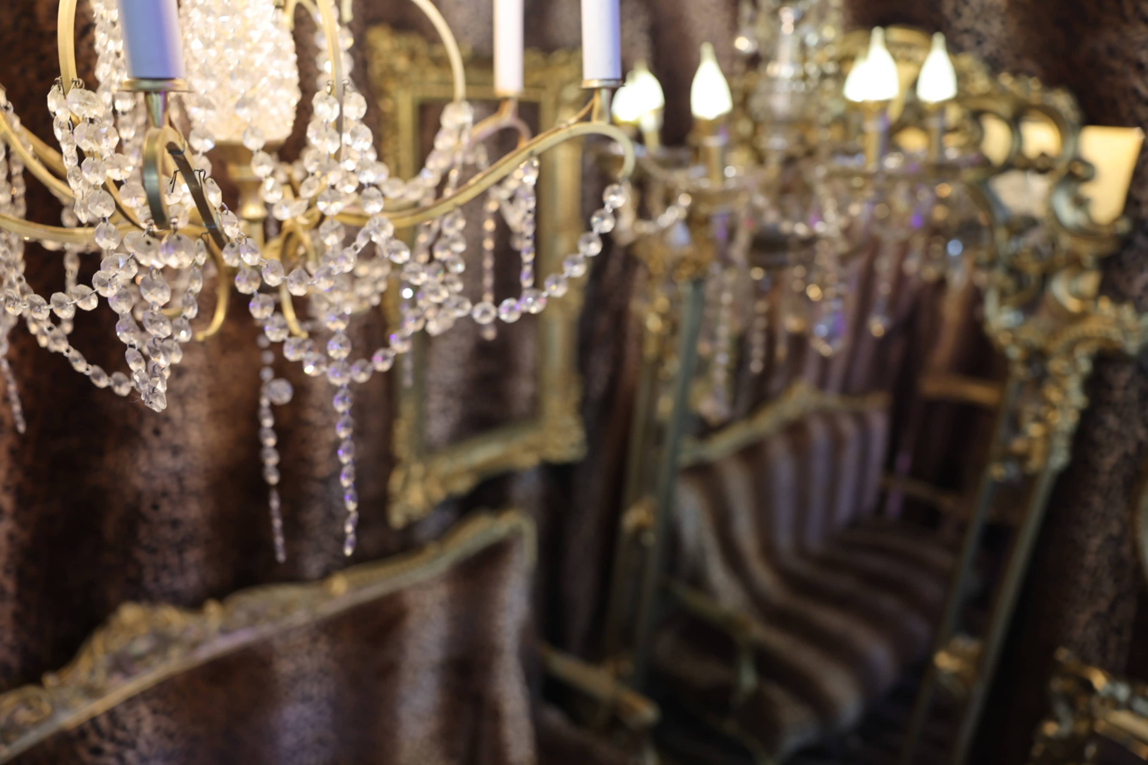 The image features an ornate chandelier with crystal accents hanging above a patterned sofa, surrounded by decorative mirrors against a textured wall.