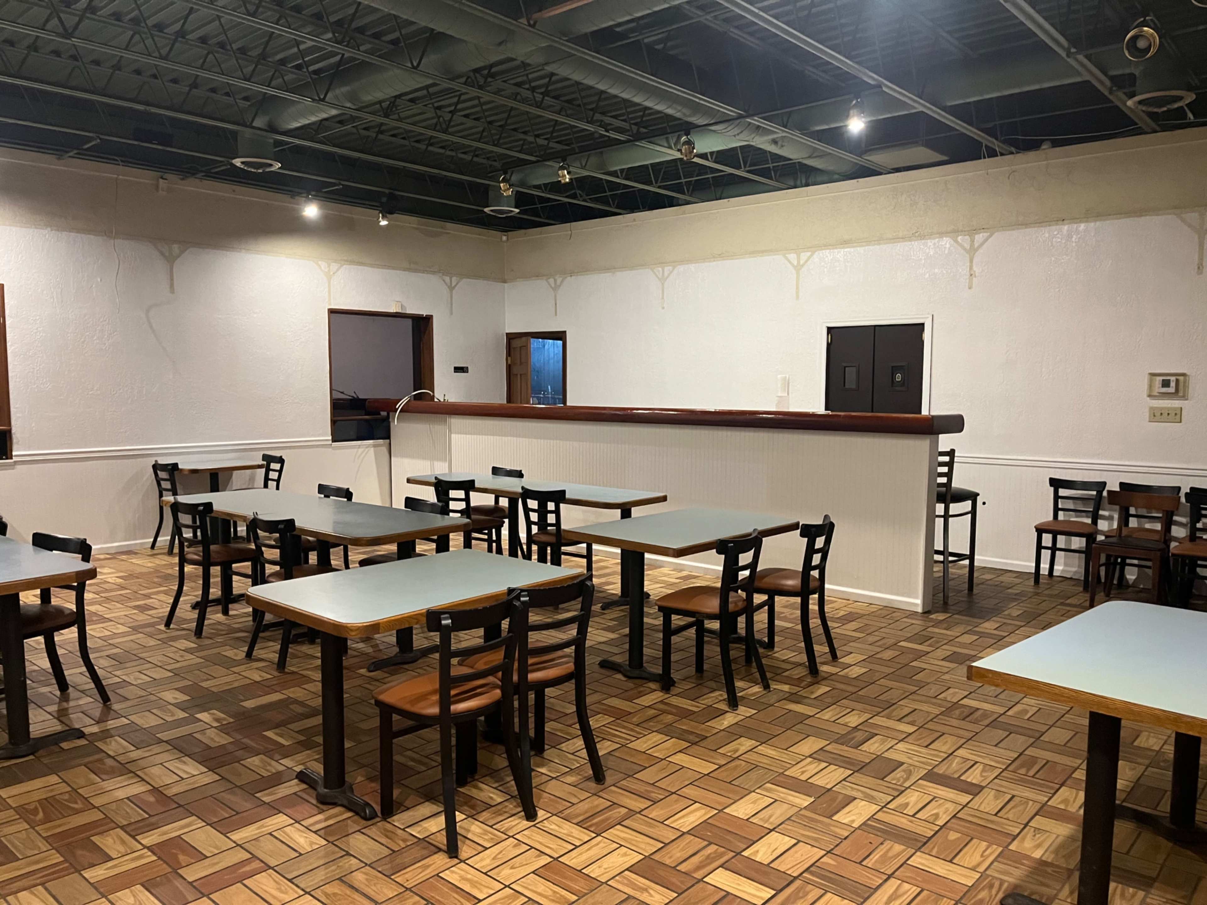 The image shows an empty indoor dining area with tables and chairs arranged in a grid pattern on a patterned floor.