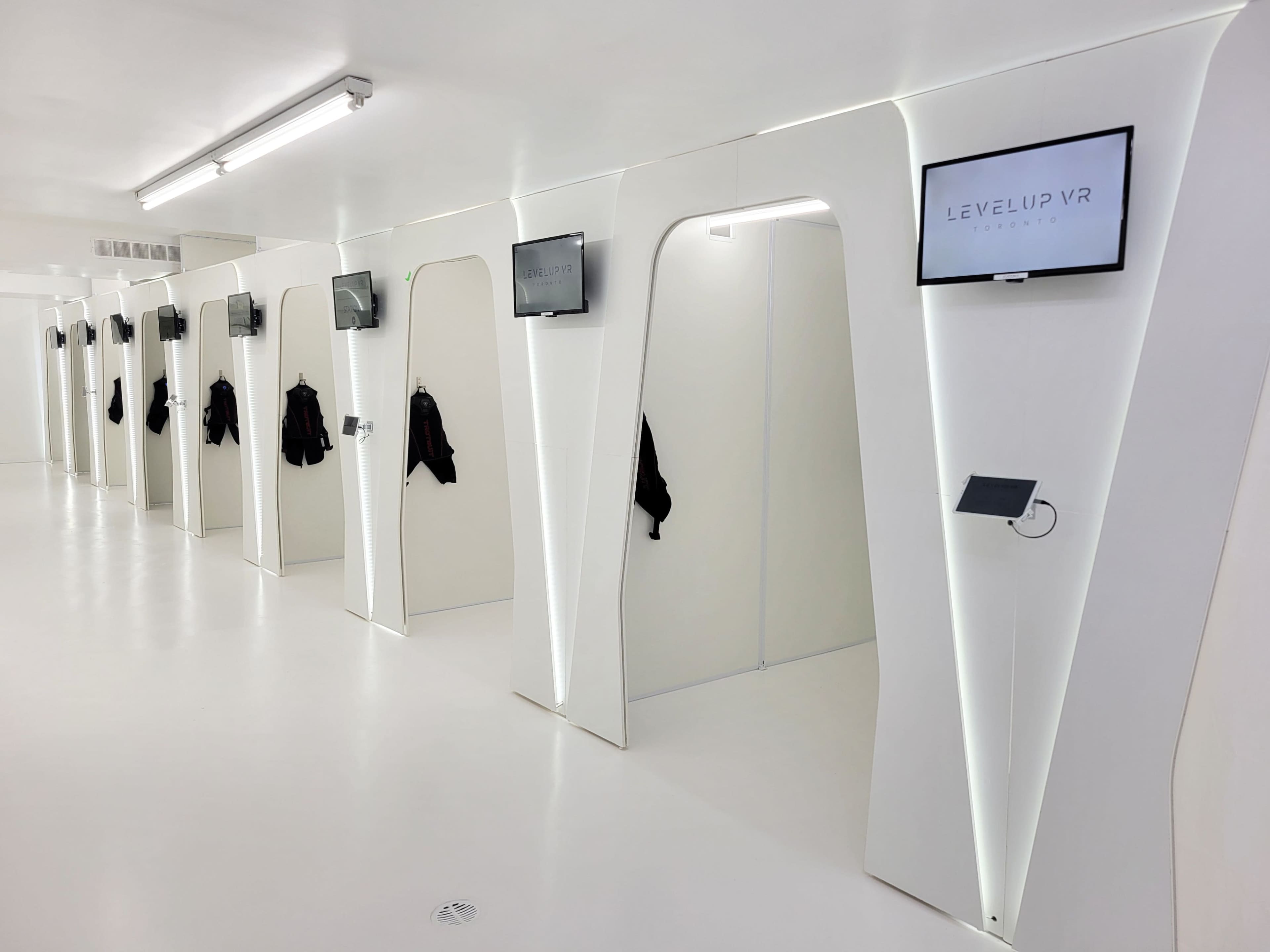 The image shows a modern VR gaming facility with several enclosed booths, each equipped with screens and displays.