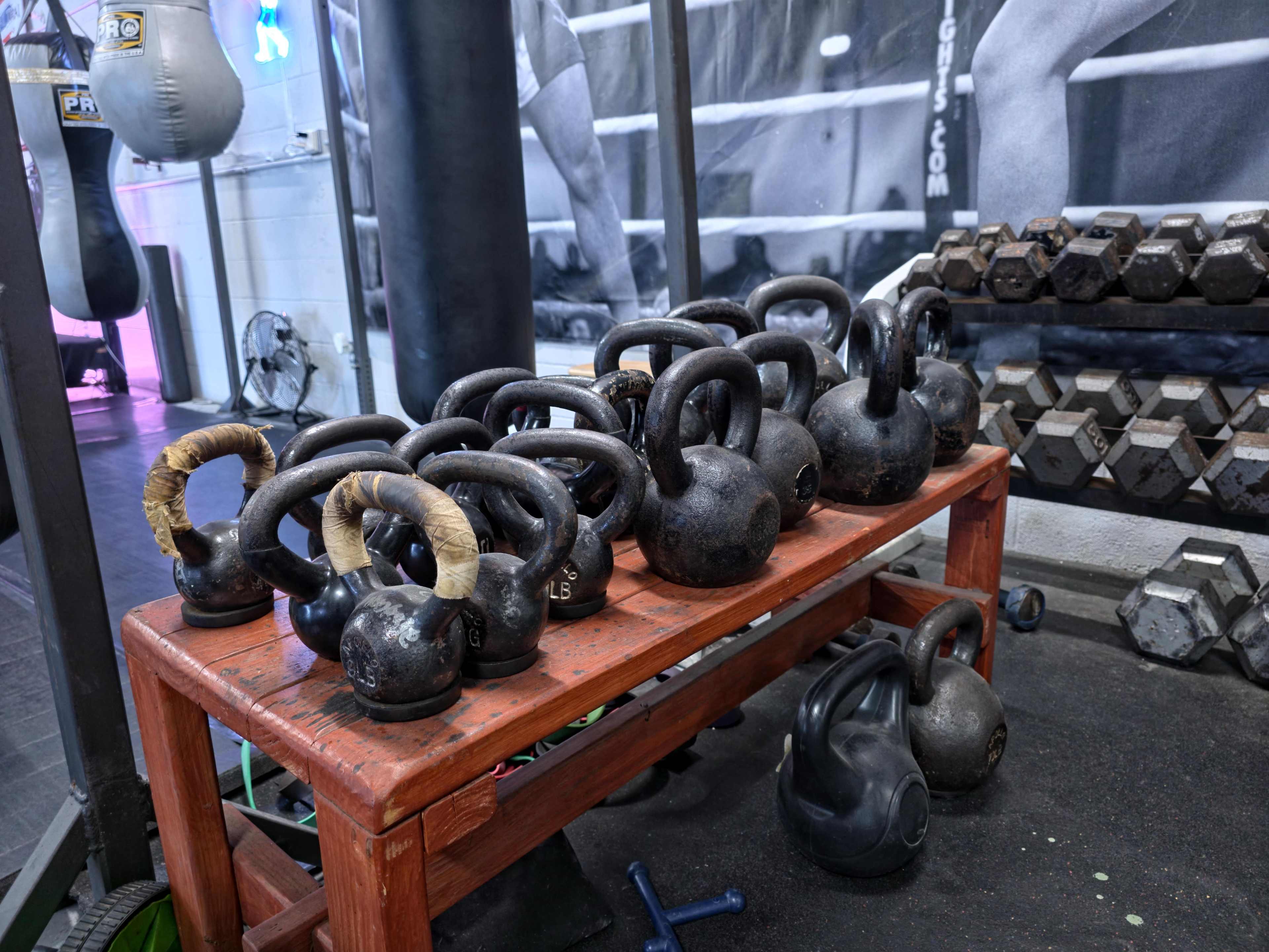 A wooden rack holds several kettlebells of various weights in a gym setting.