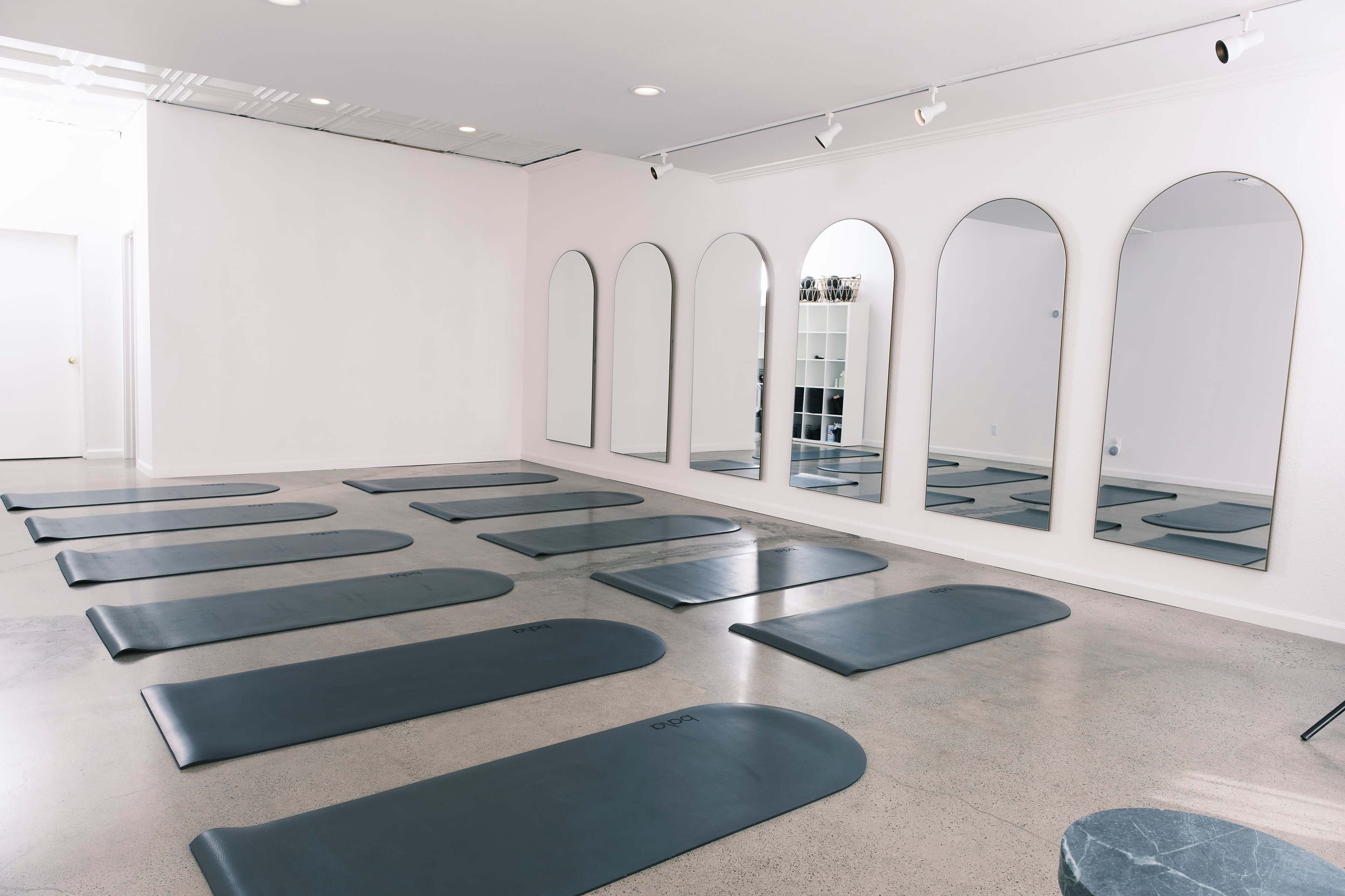 A yoga studio with several exercise mats arranged on the floor and large arched mirrors mounted on the wall.
