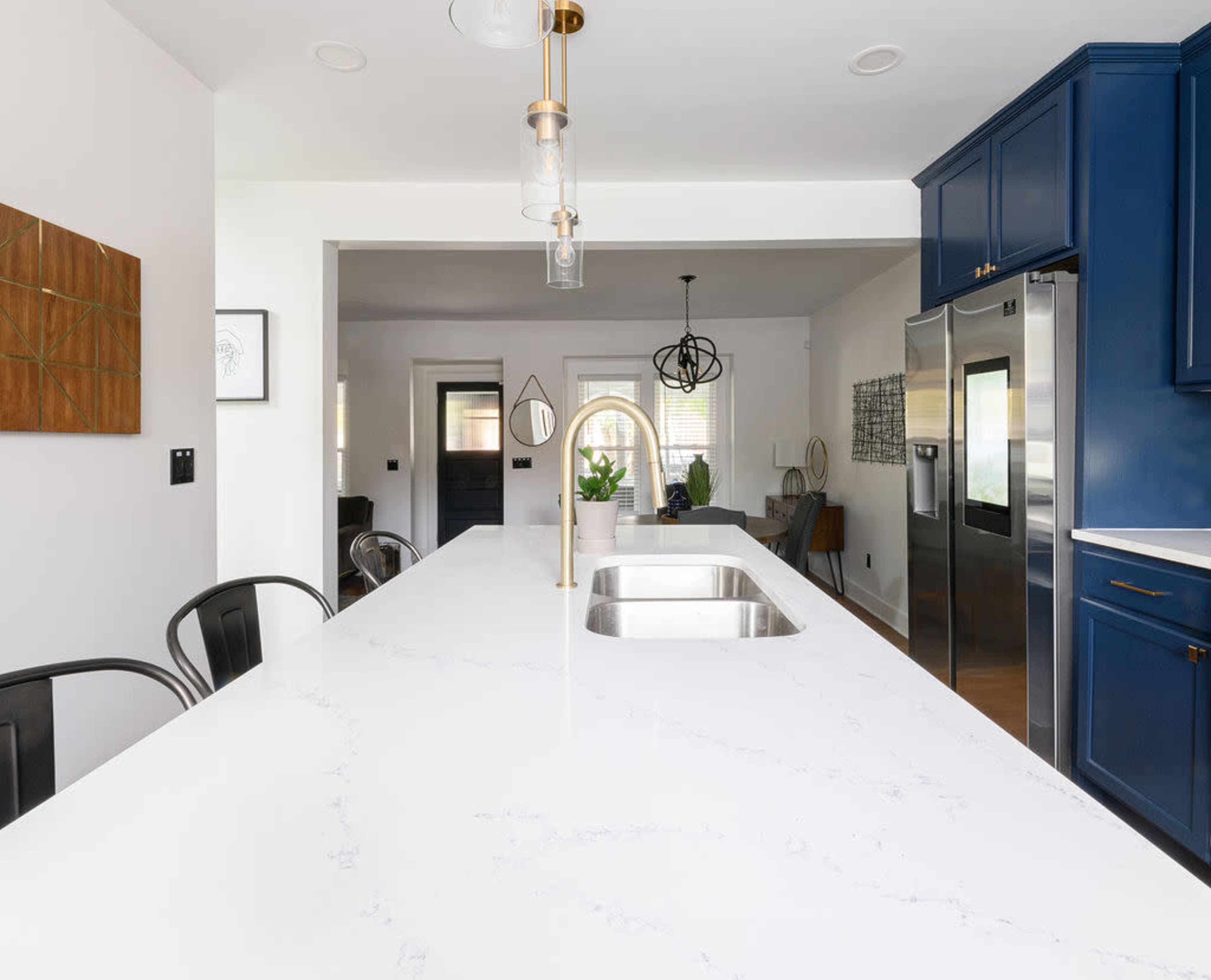 A modern kitchen with a large white countertop, blue cabinetry, and stainless steel appliances.