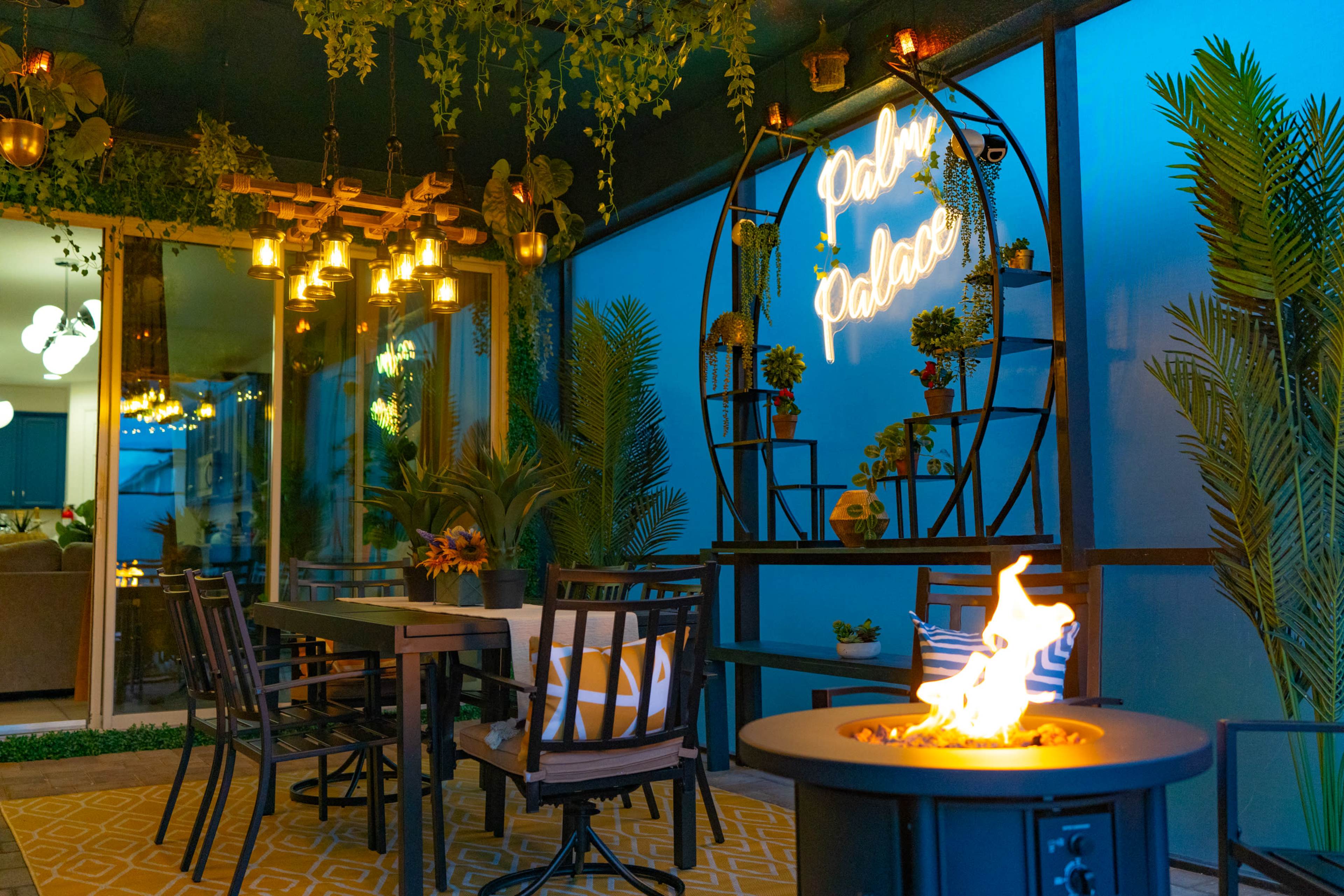 A cozy outdoor dining area featuring black tables and chairs, decorative plants, and a neon sign that reads "Palace."