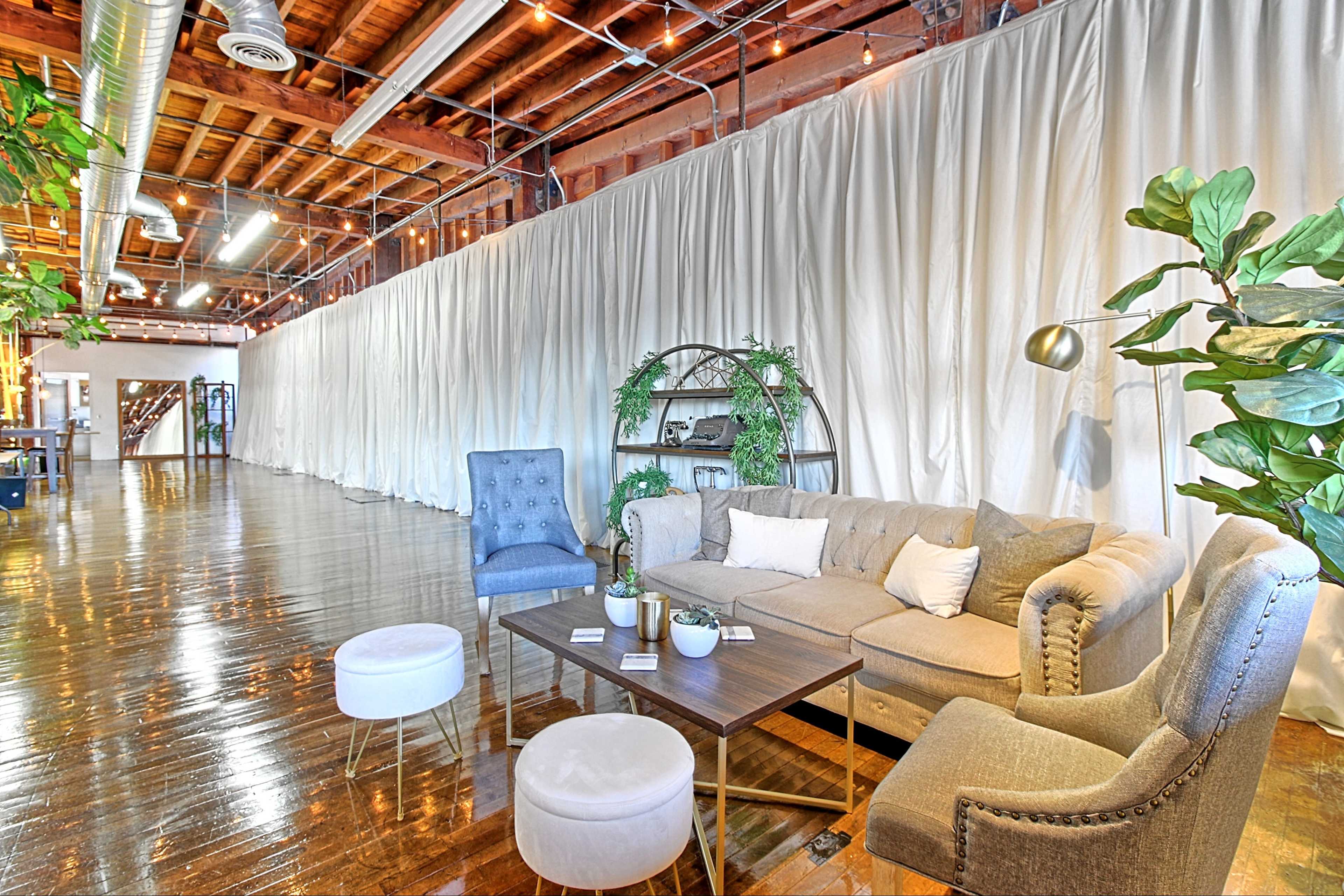 A spacious interior with polished wood floors, a large white curtain backdrop, and a cozy seating area containing a sofa, armchairs, and a coffee table.