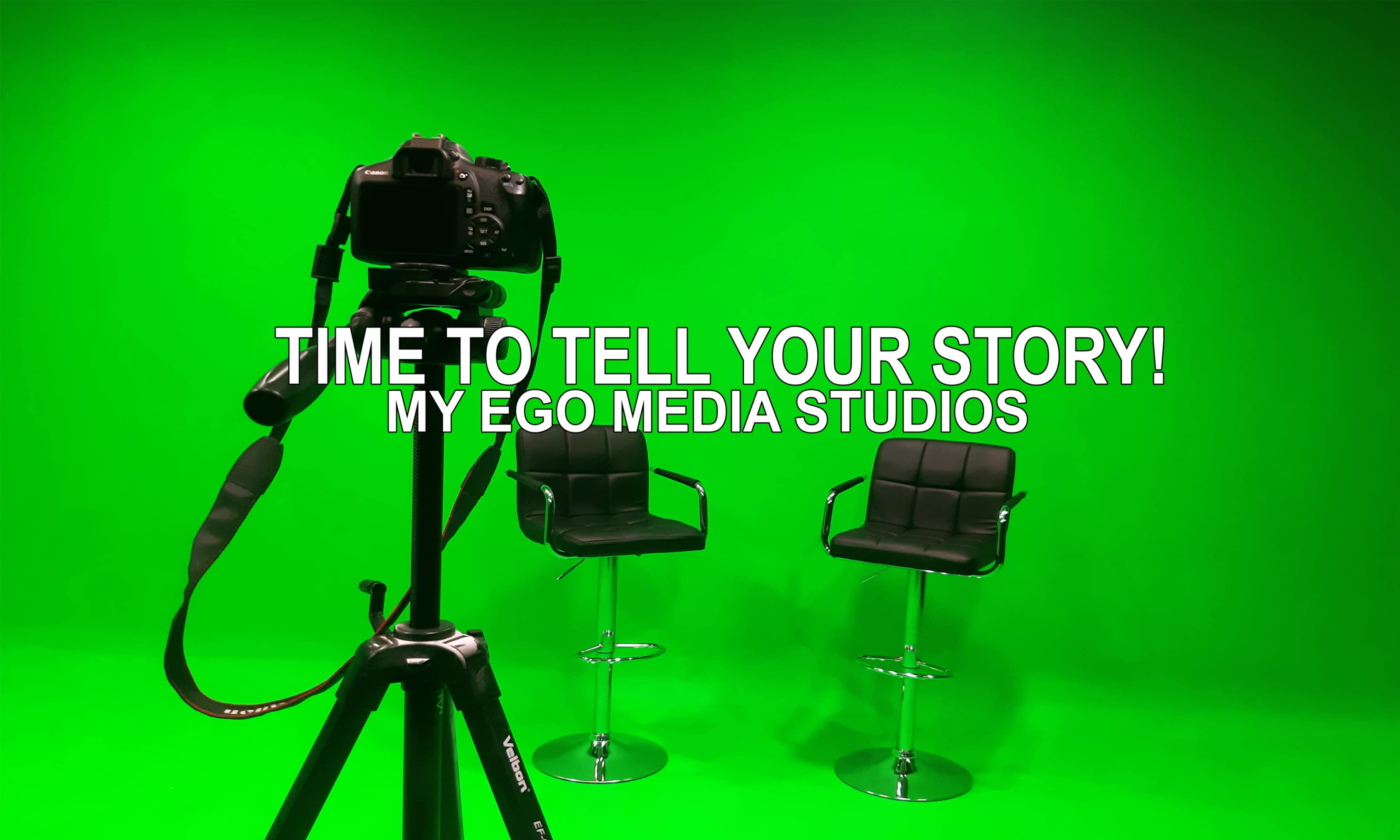 A camera is positioned on a tripod facing two empty black chairs in front of a green backdrop at My Ego Media Studios.