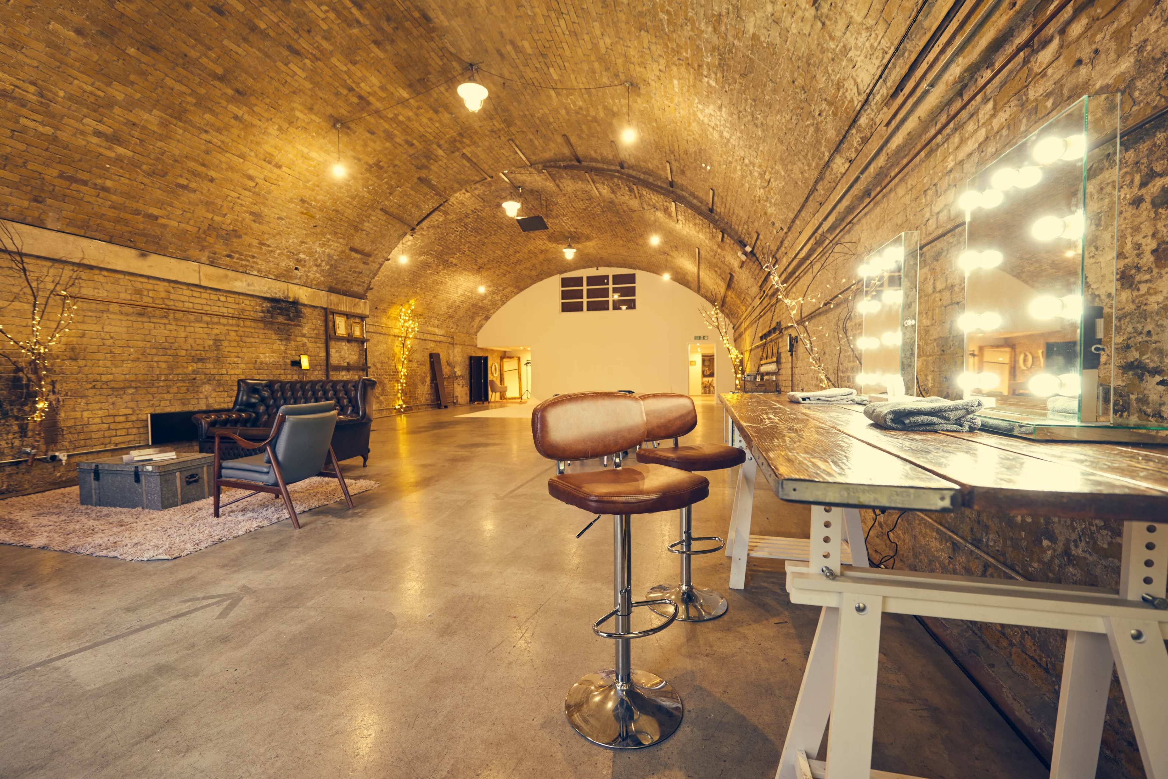 The image shows a spacious, arched interior with exposed brick walls, a bar area with tall stools, and soft lighting enhancing the overall ambiance.
