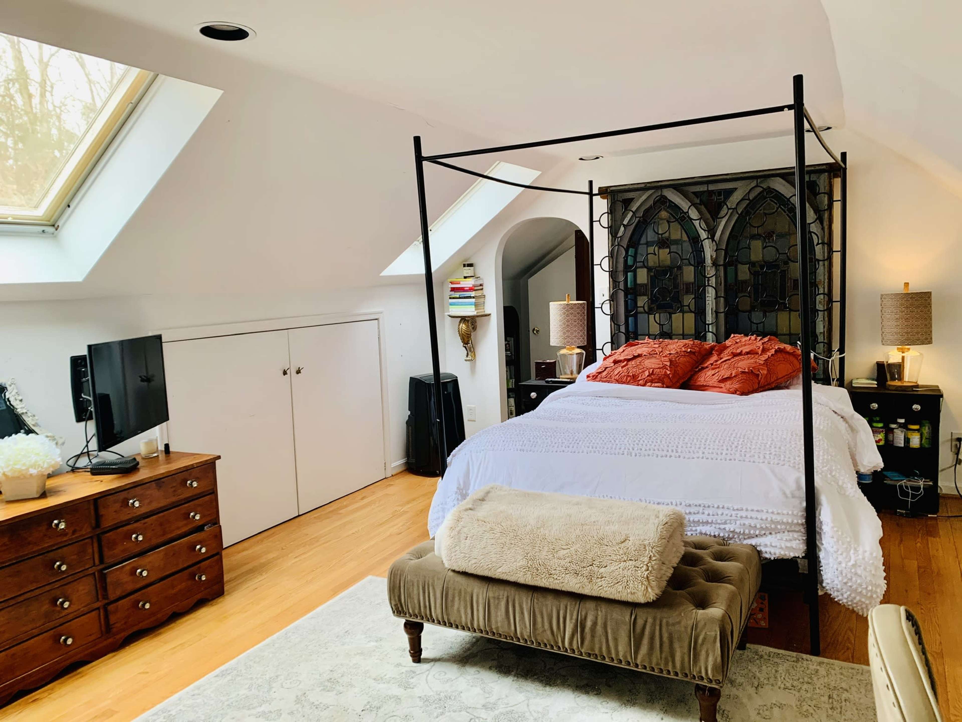 A spacious bedroom featuring a four-poster bed, a dresser, and a skylight illuminating the room.
