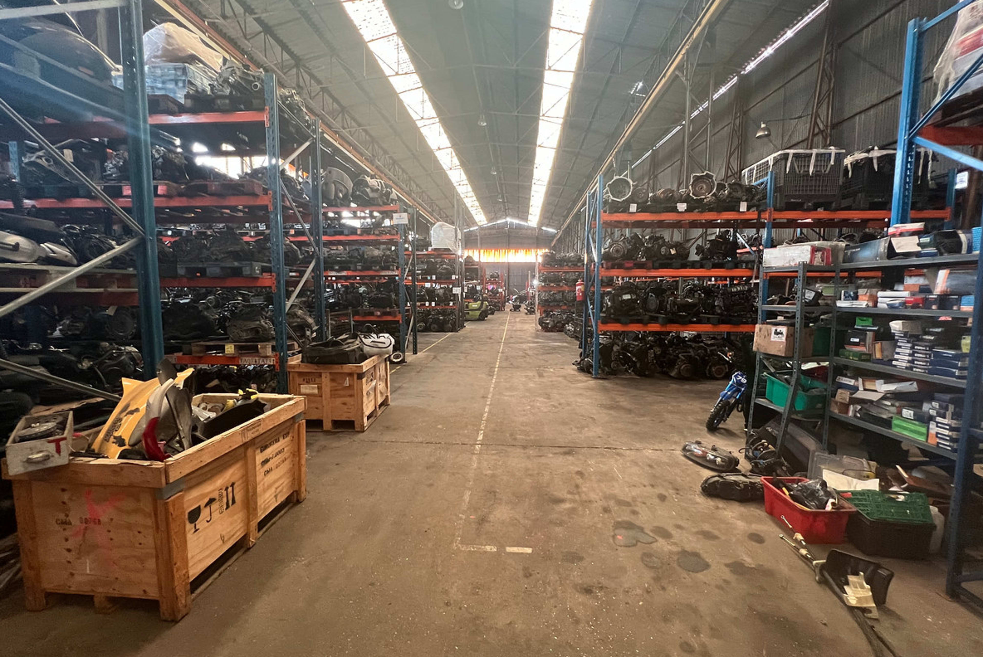 An organized warehouse filled with shelves of motorcycle parts and accessories, with a clear walkway in the center.