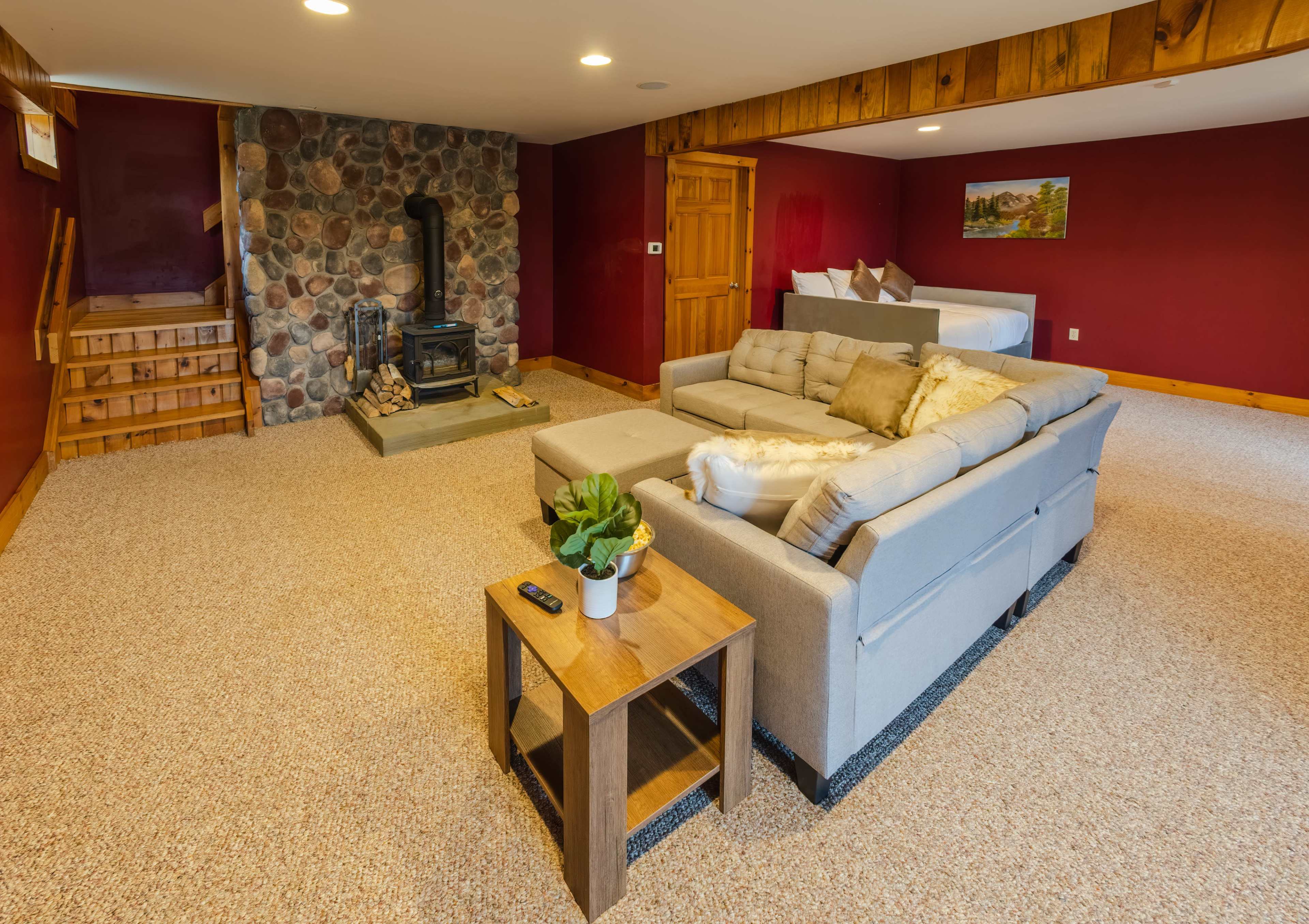 A spacious, cozy basement living area featuring a beige sofa, a wooden coffee table with a plant, and a stone fireplace.