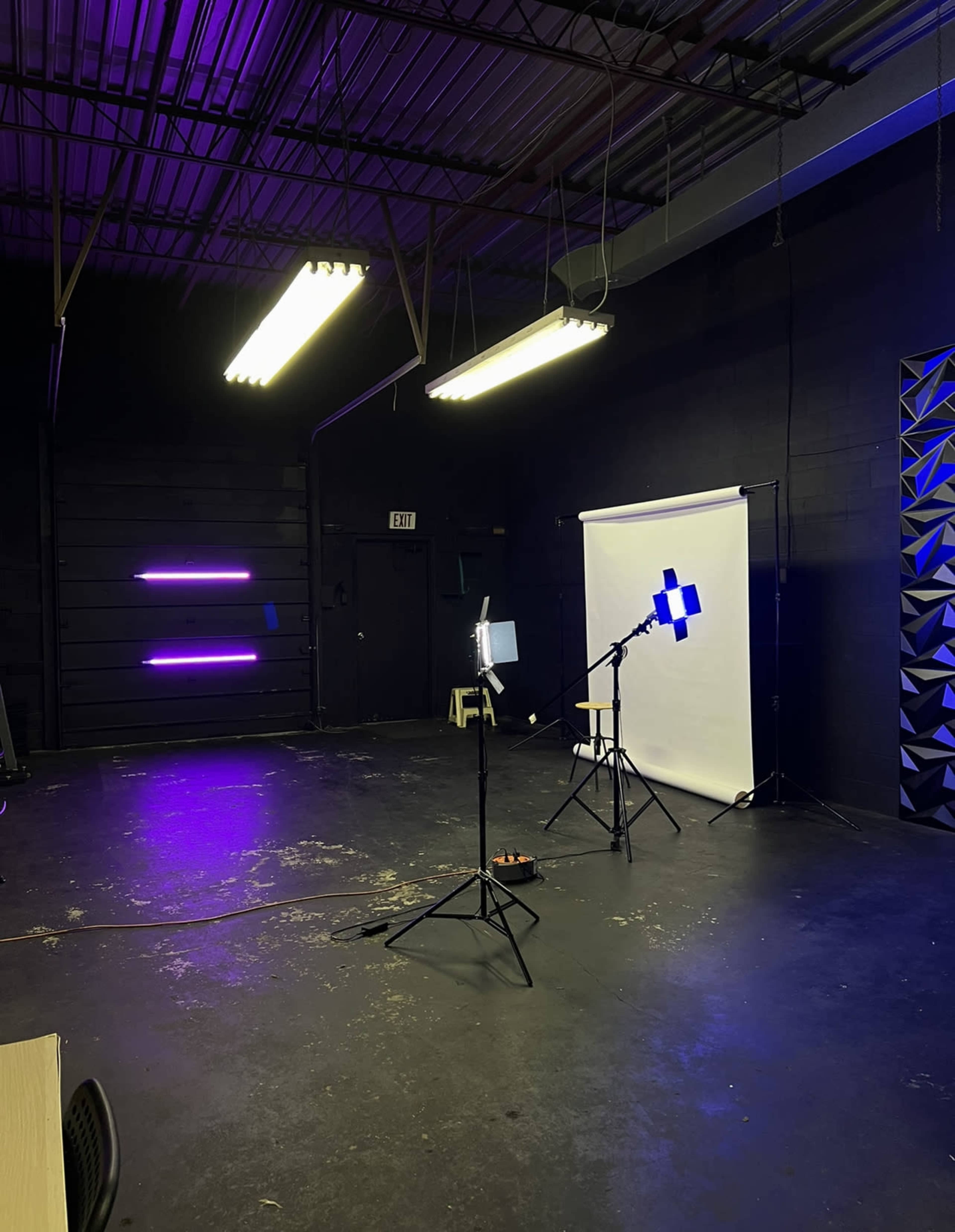 The image shows a studio setup with a white backdrop, a microphone on a stand, and several lighting fixtures in a dimly lit room.