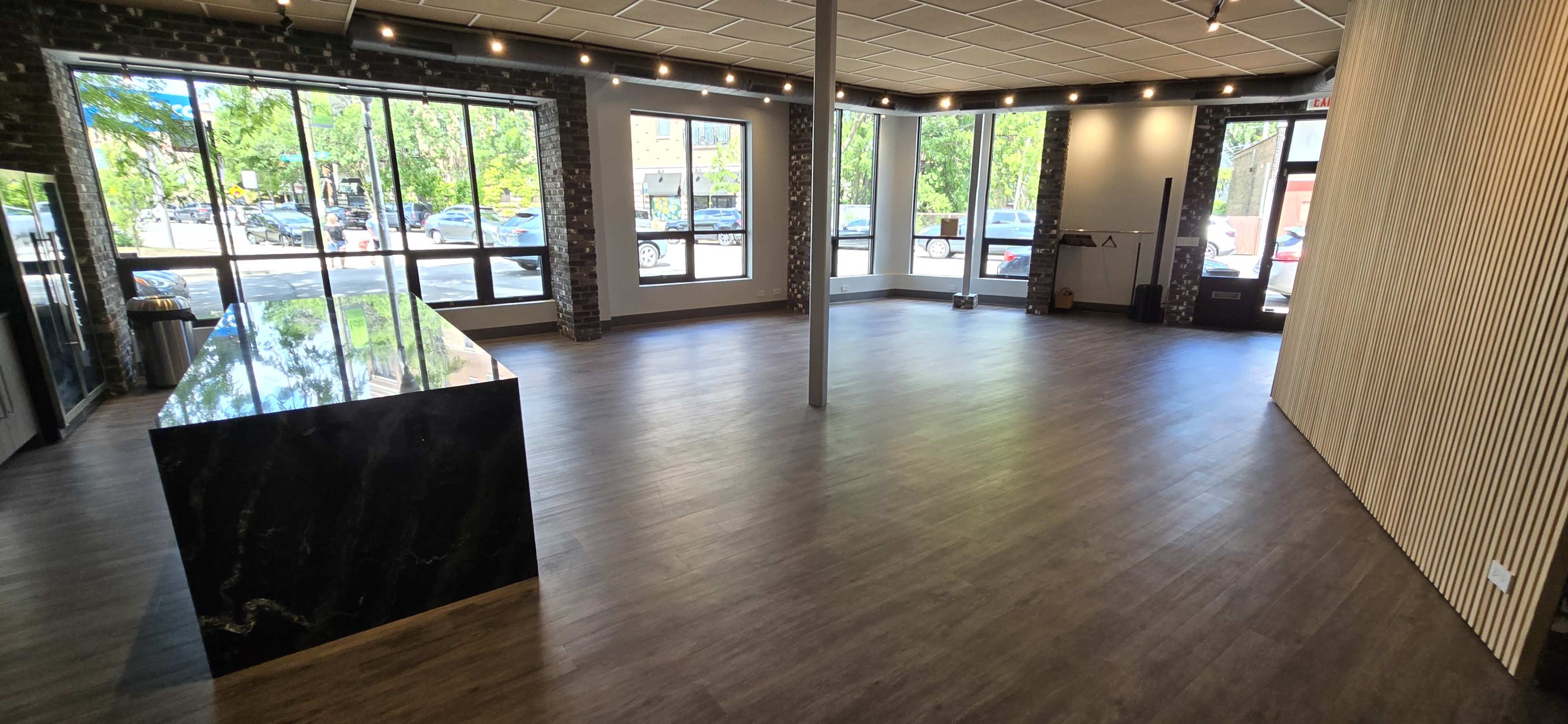 A spacious, empty interior with large windows, a dark marble counter on one side, and wooden flooring.