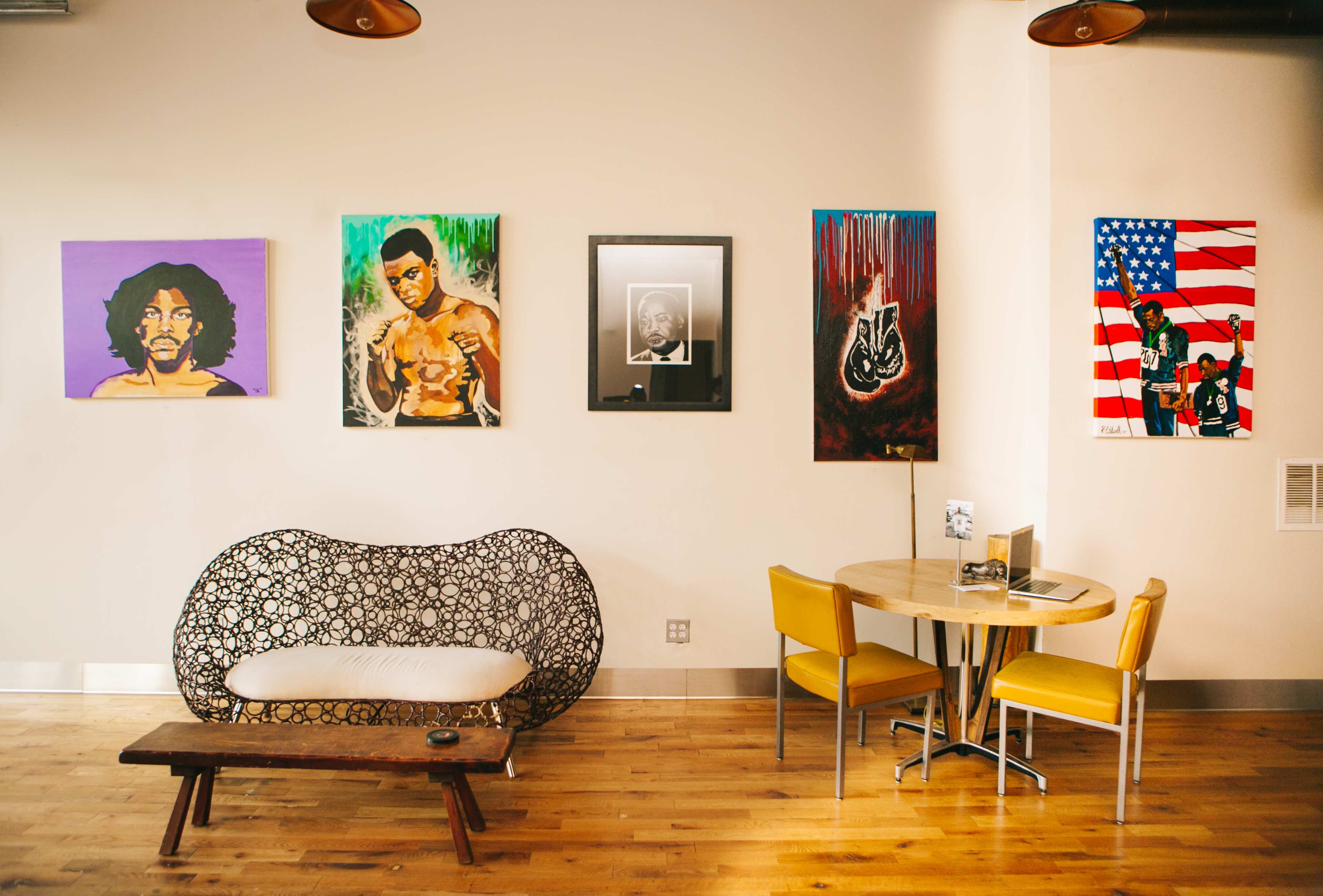 A modern café interior featuring an artistic wall with vibrant paintings of musicians and a cozy seating area with a round table and chairs.