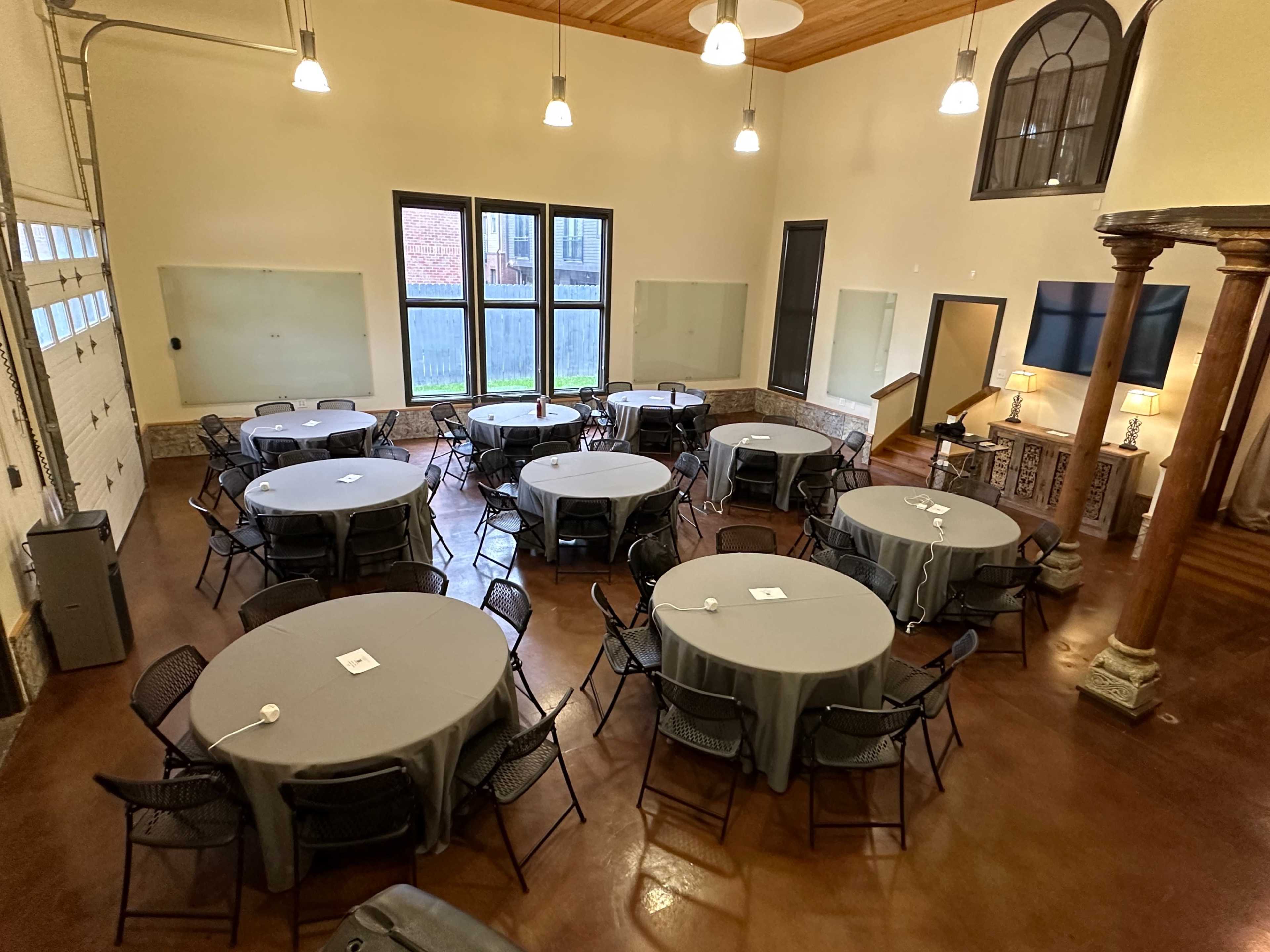 A large, well-lit room arranged with several round tables covered in gray tablecloths and surrounded by black chairs.