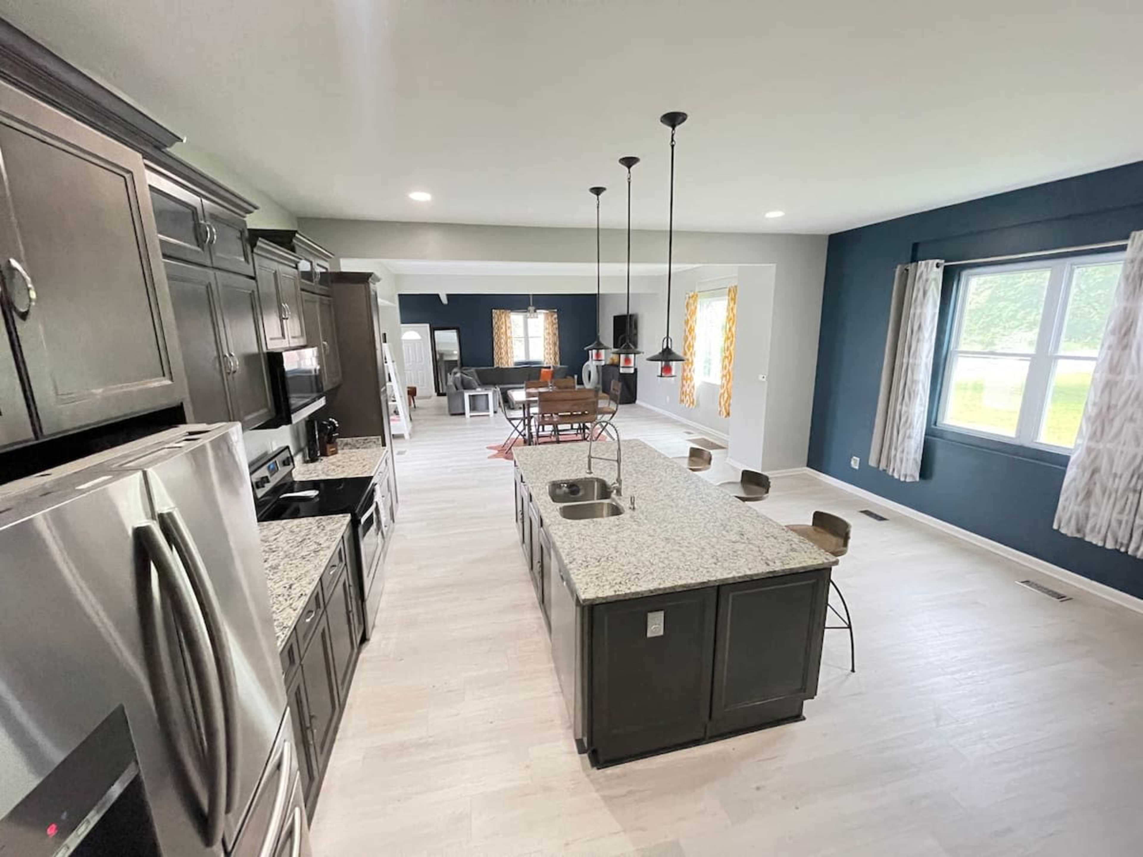 A modern kitchen featuring dark cabinetry, granite countertops, and an island with seating, open to a dining area with a table and chairs.