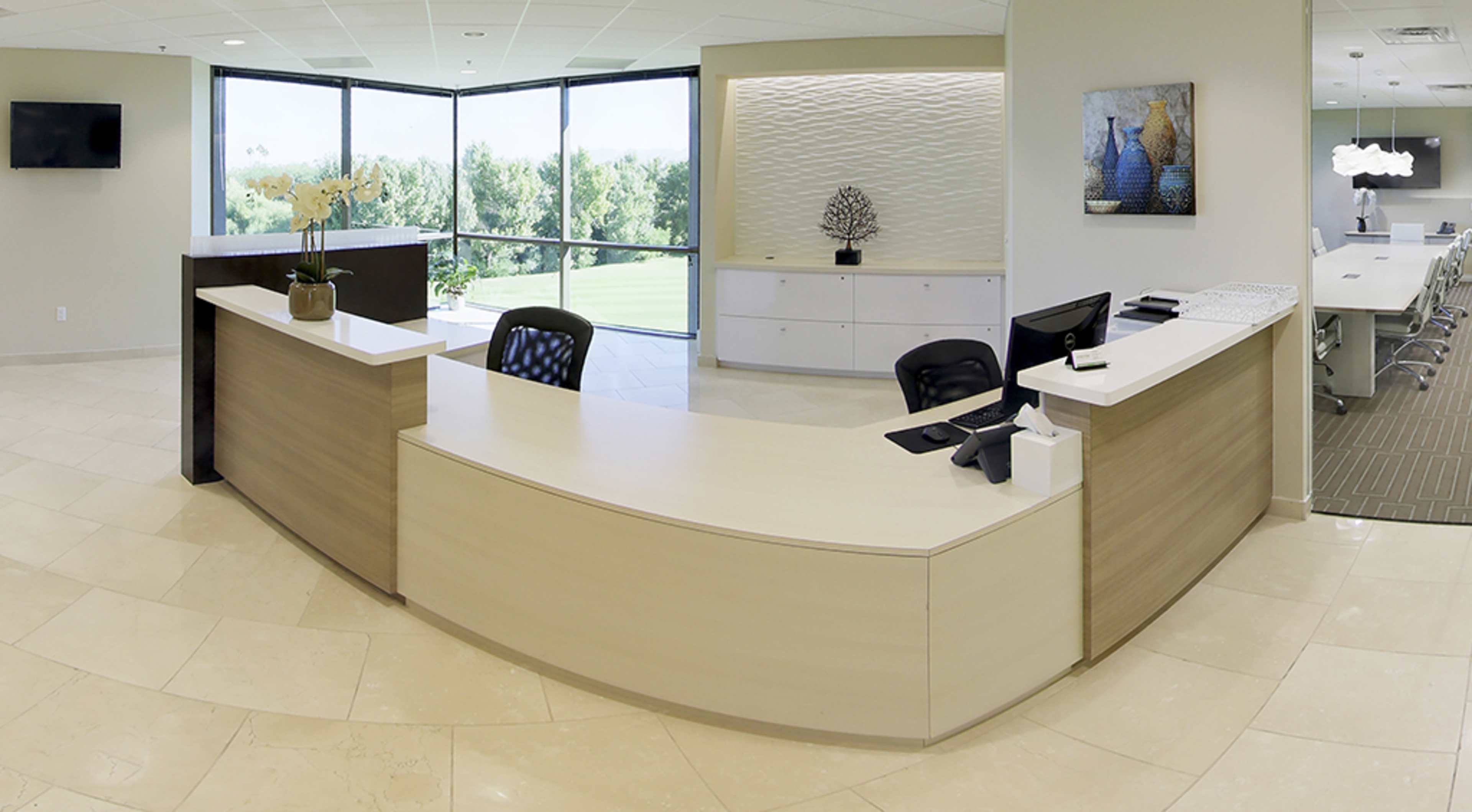A modern reception area with a curved front desk, a large window providing views of greenery, and a conference room in the background.