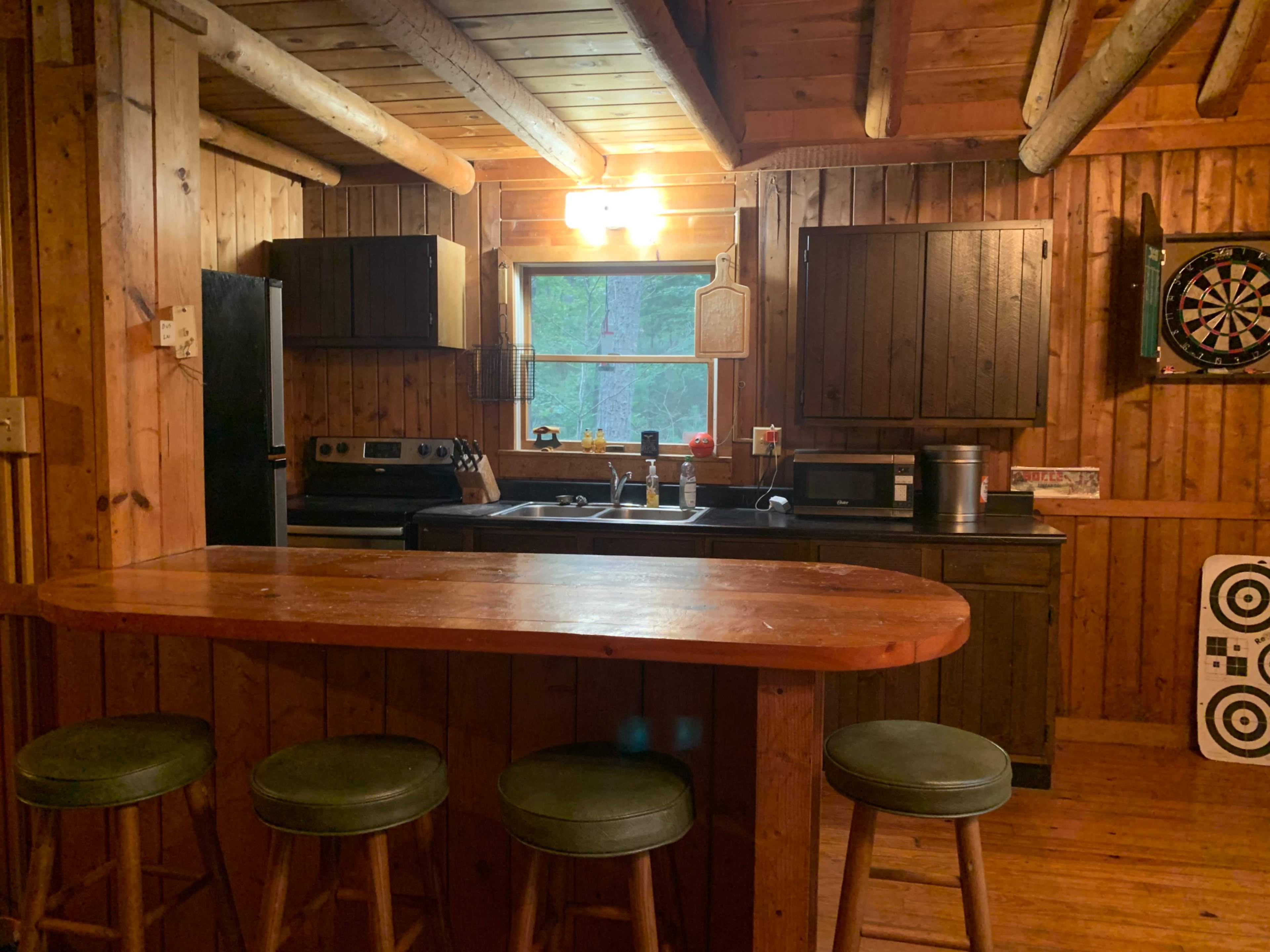 A rustic wooden kitchen with dark cabinets, a stove, and a bar with four stools.