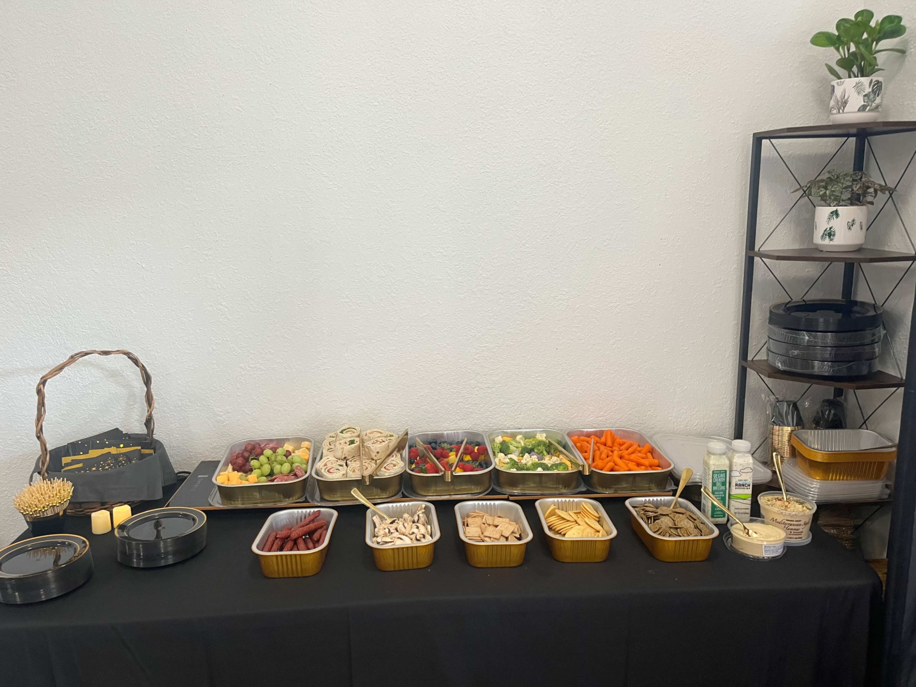 The image shows a buffet-style arrangement of various food items, including fruits, vegetables, and snacks, displayed on a black tablecloth.