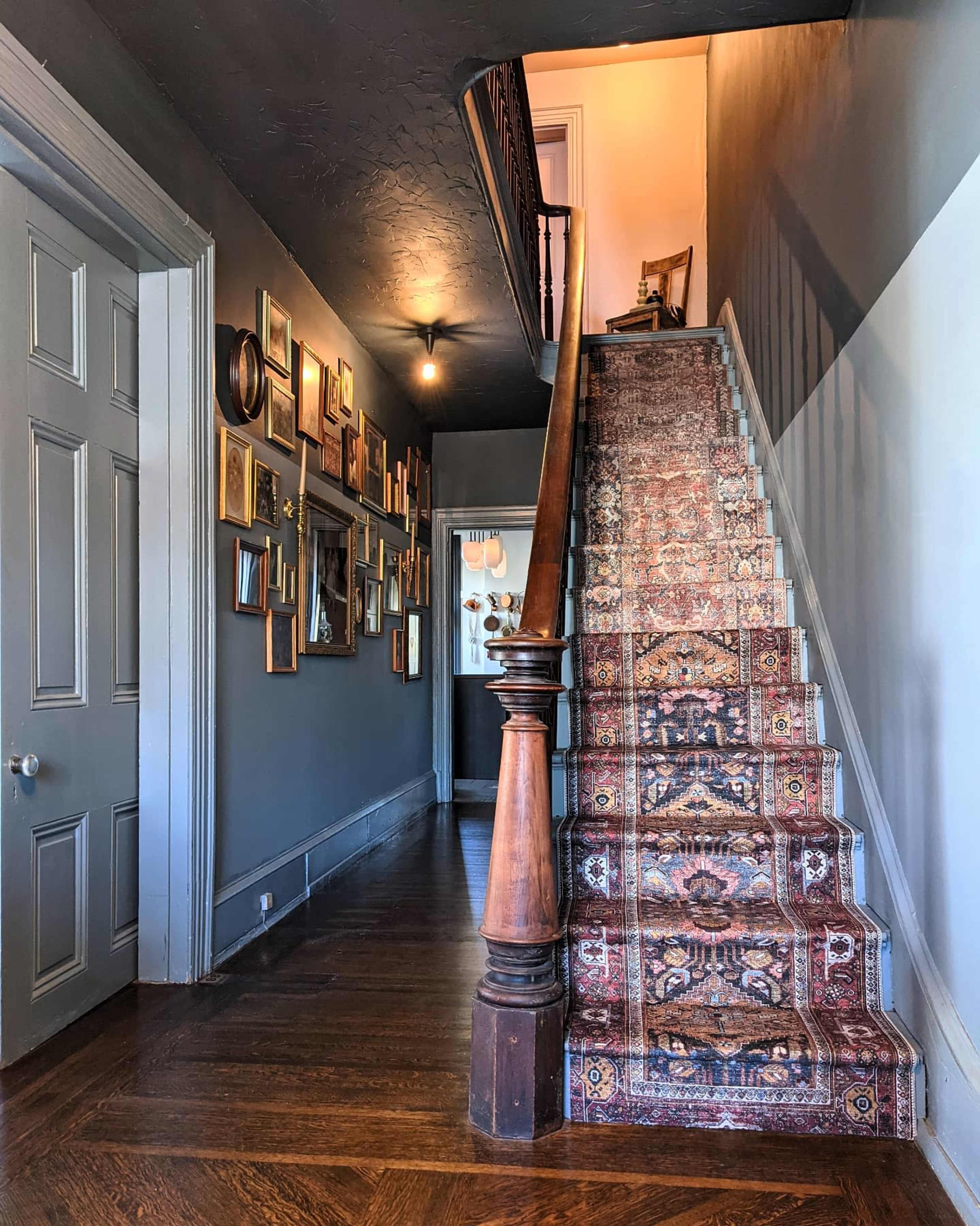 A hallway with a staircase featuring a patterned carpet runner and a gallery wall of framed pictures on the left side.