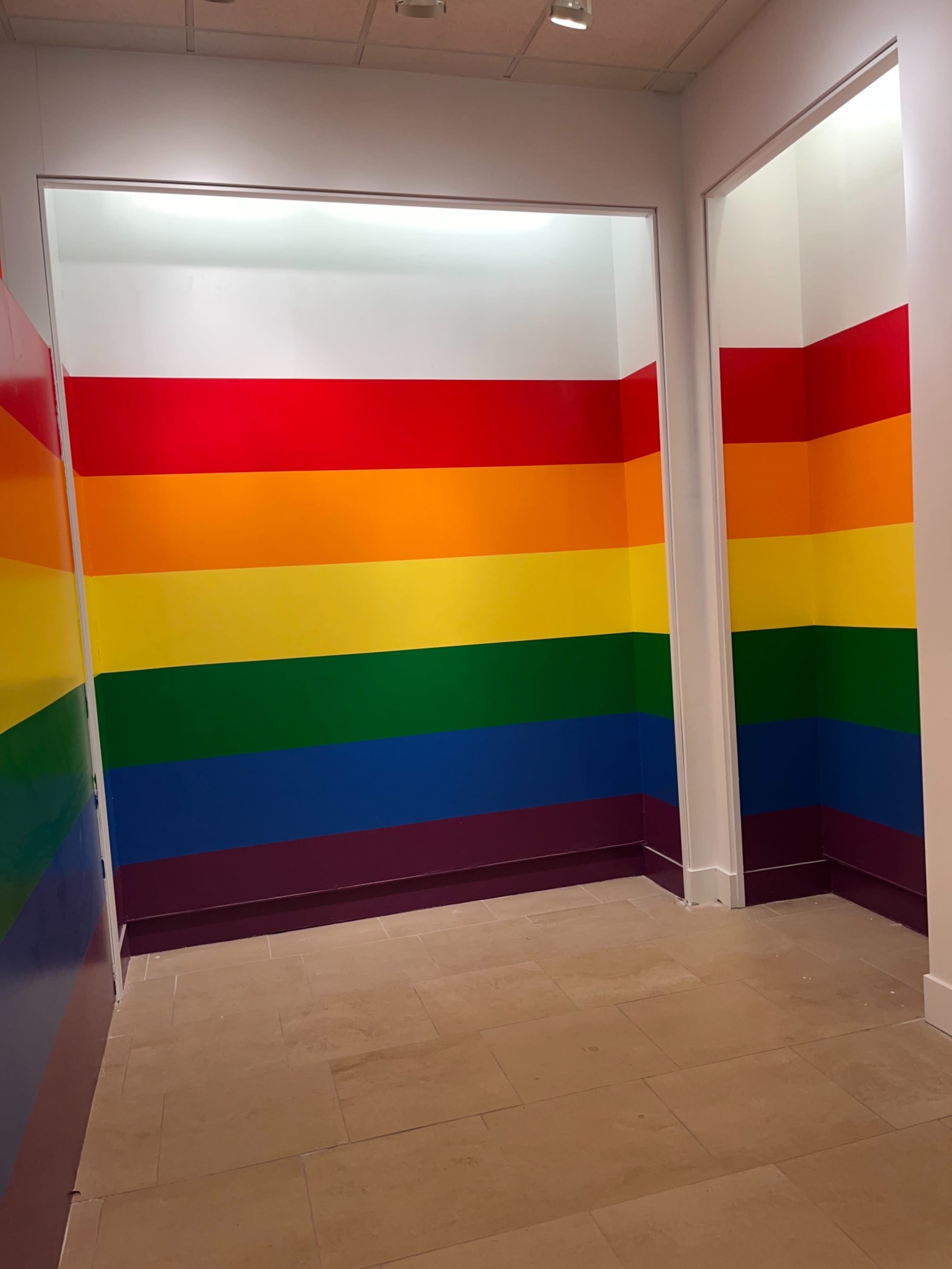 A corner of a room with walls painted in horizontal stripes of rainbow colors.