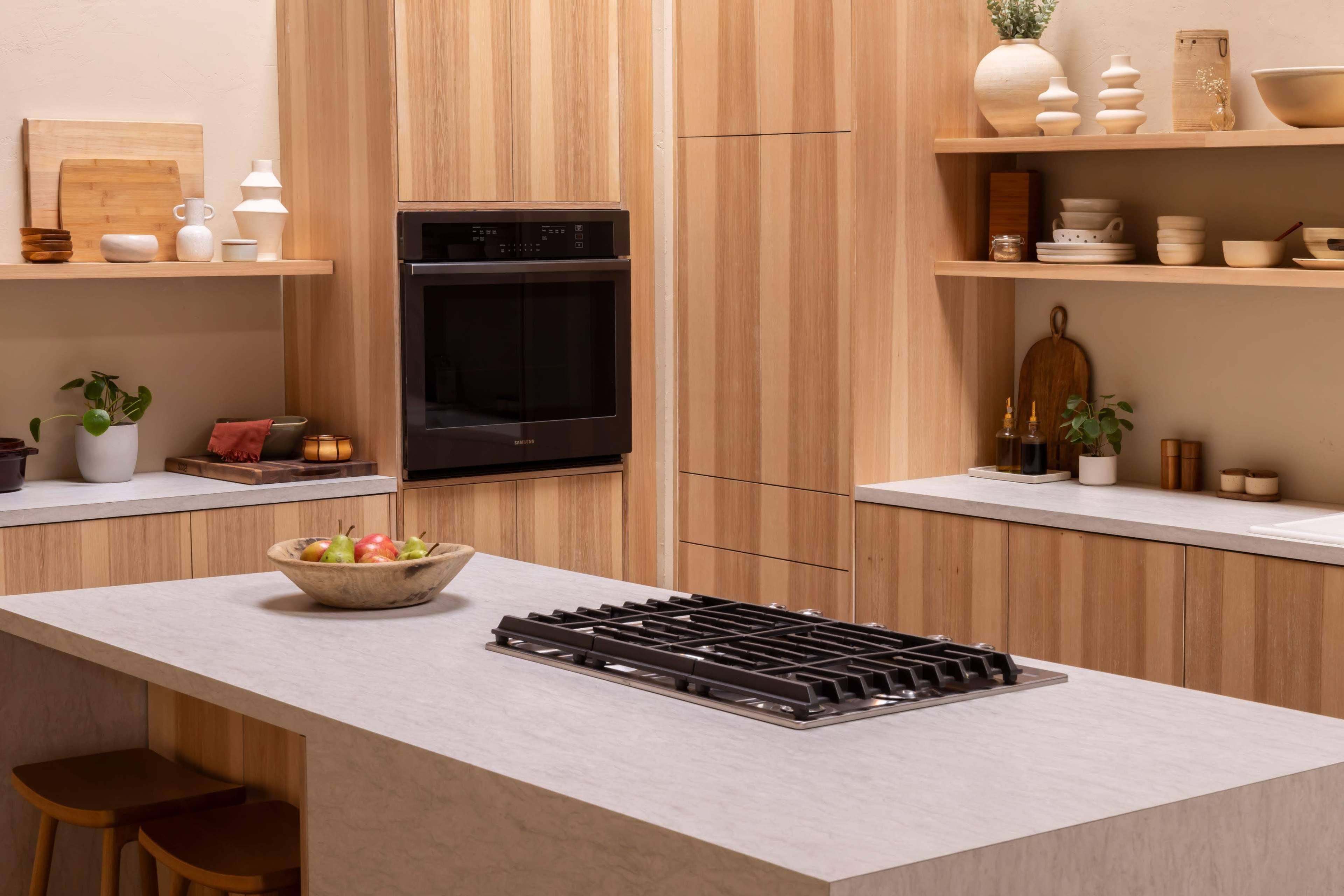 A modern kitchen features wooden cabinetry, a central island with a stovetop, and neatly arranged decorative items on the shelves.