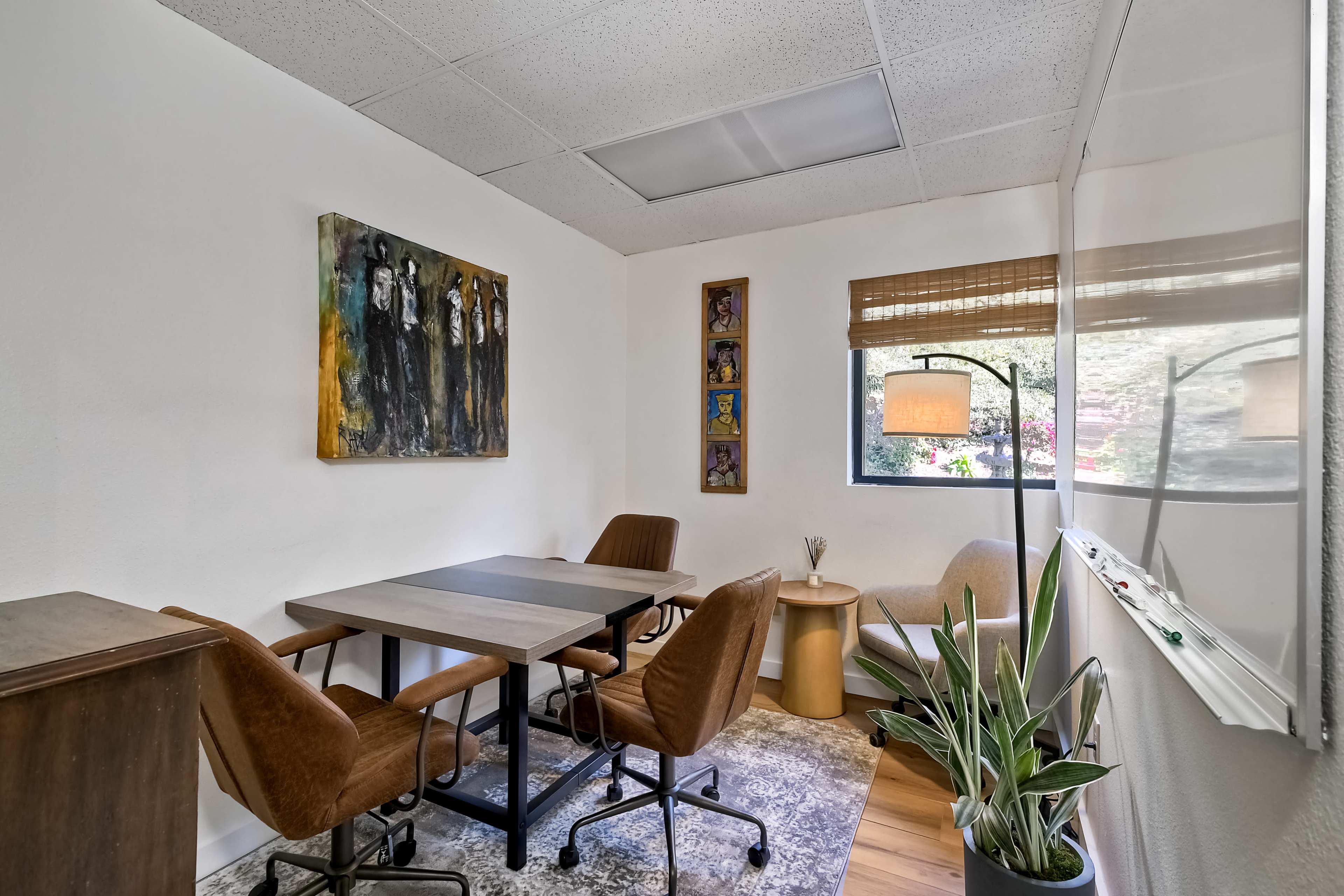 The image shows a small meeting room with a table, several chairs, and a window displaying natural light.