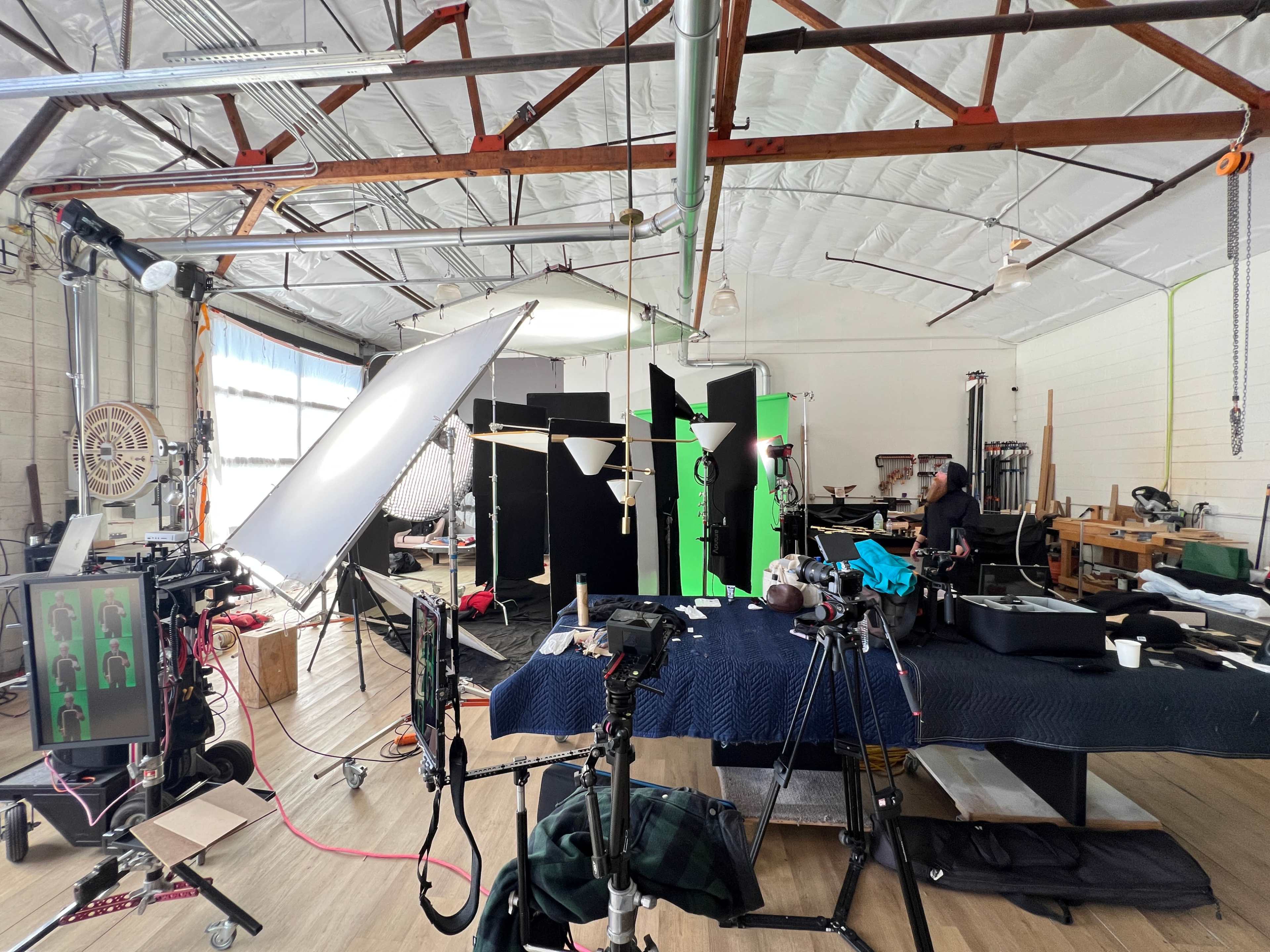 The image shows a well-equipped studio space with various lighting and filming equipment, including a large reflector and green screens set up for a production.