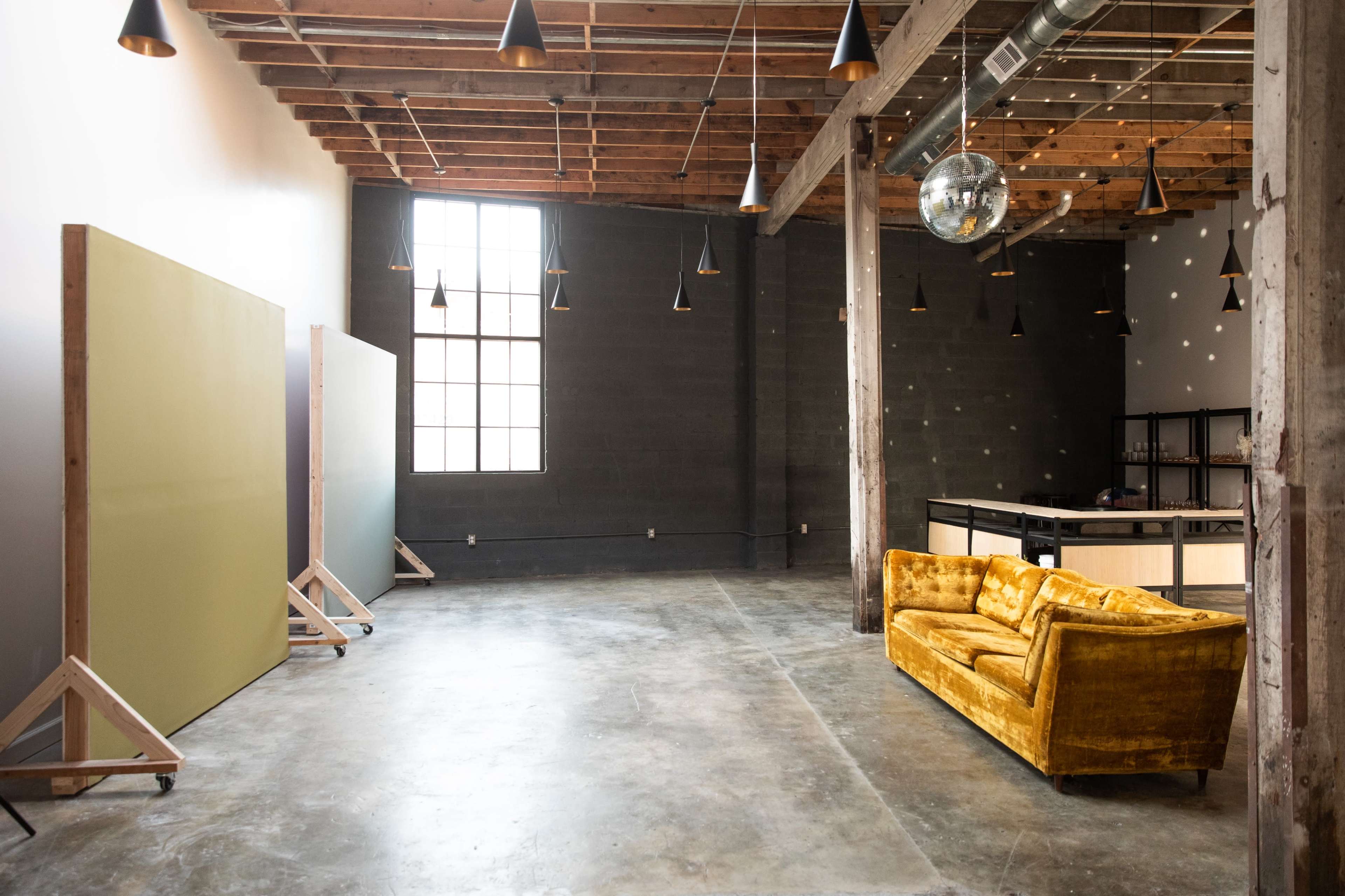 A spacious room features a yellow couch, large green panels on wooden stands, and a disco ball hanging from the ceiling.