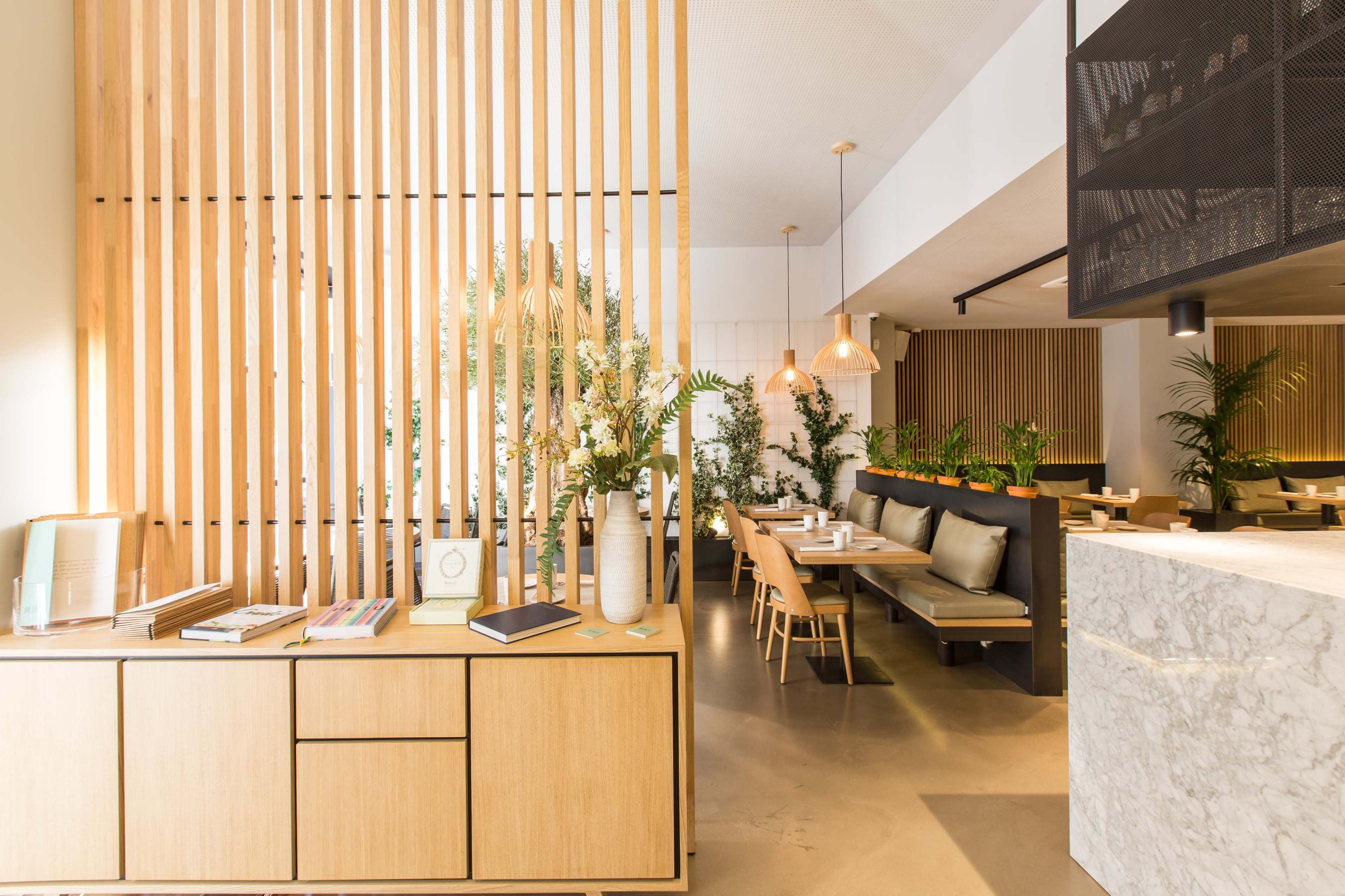 A modern restaurant interior with wooden slat partitions, lush planters, and a mix of dining tables and seating areas.
