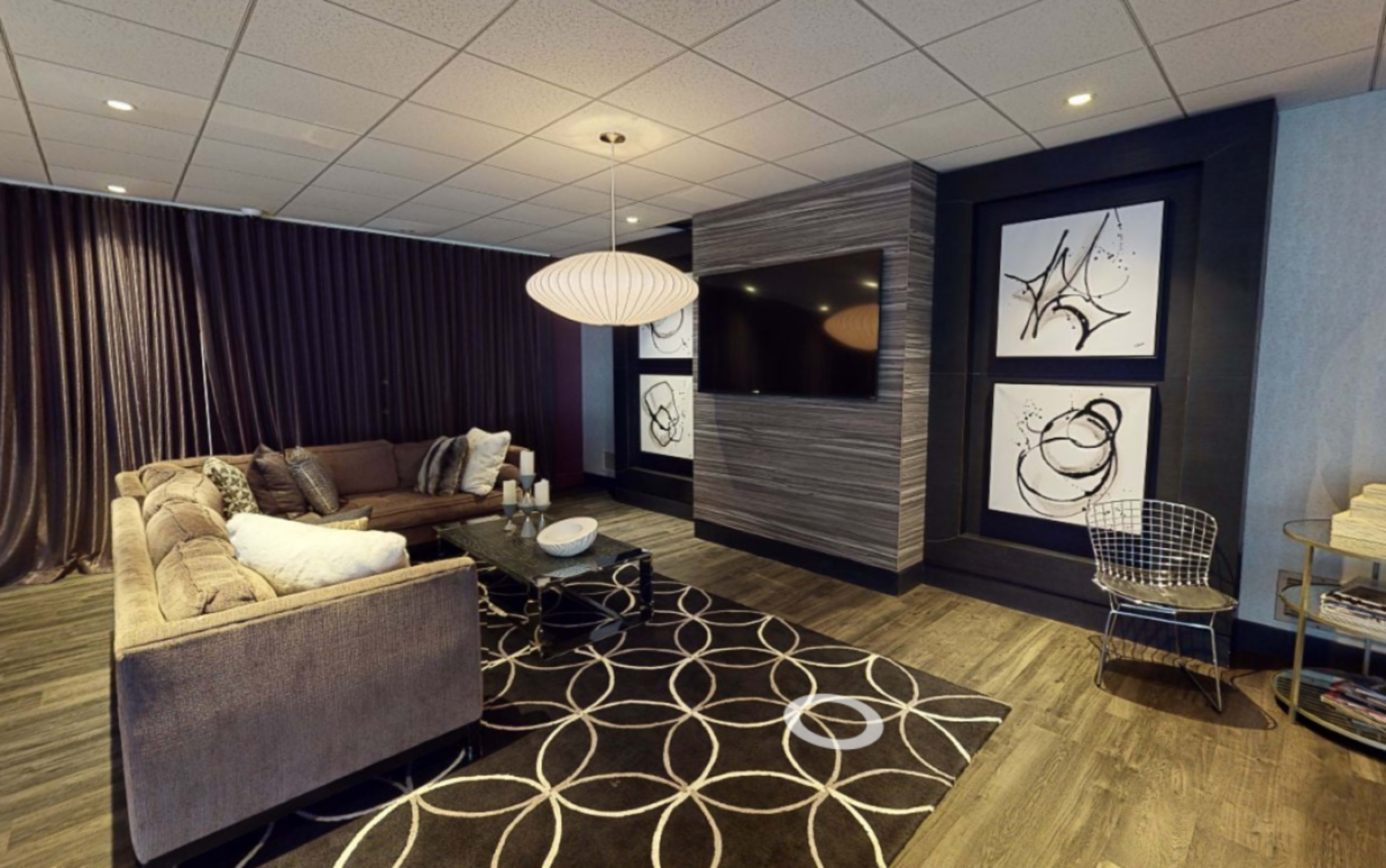 A modern lounge area with a plush sectional sofa, a circular rug, a wall-mounted television, and abstract artwork framed on the walls.