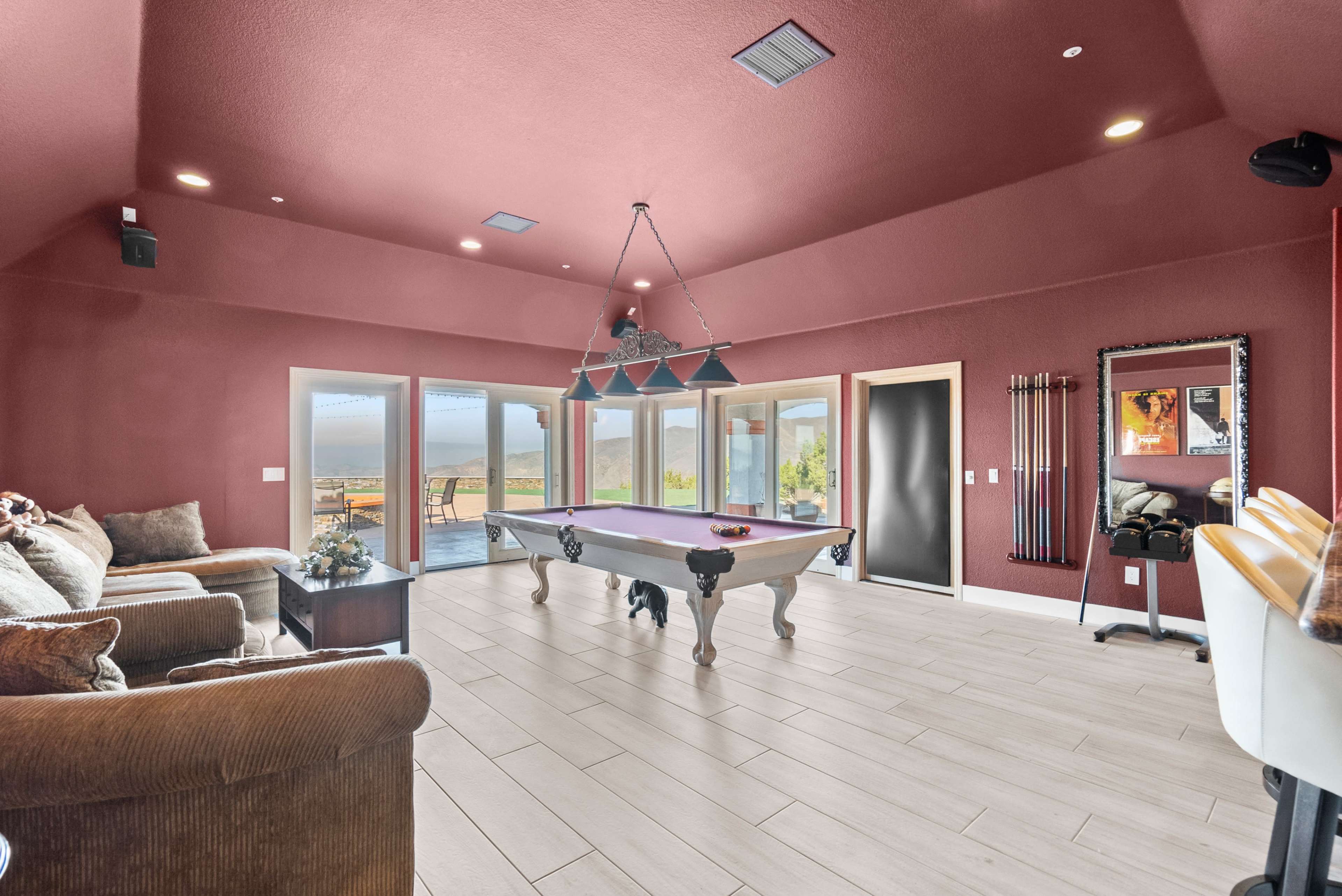 A spacious game room features a billiards table, comfortable seating, and large windows that provide scenic views.