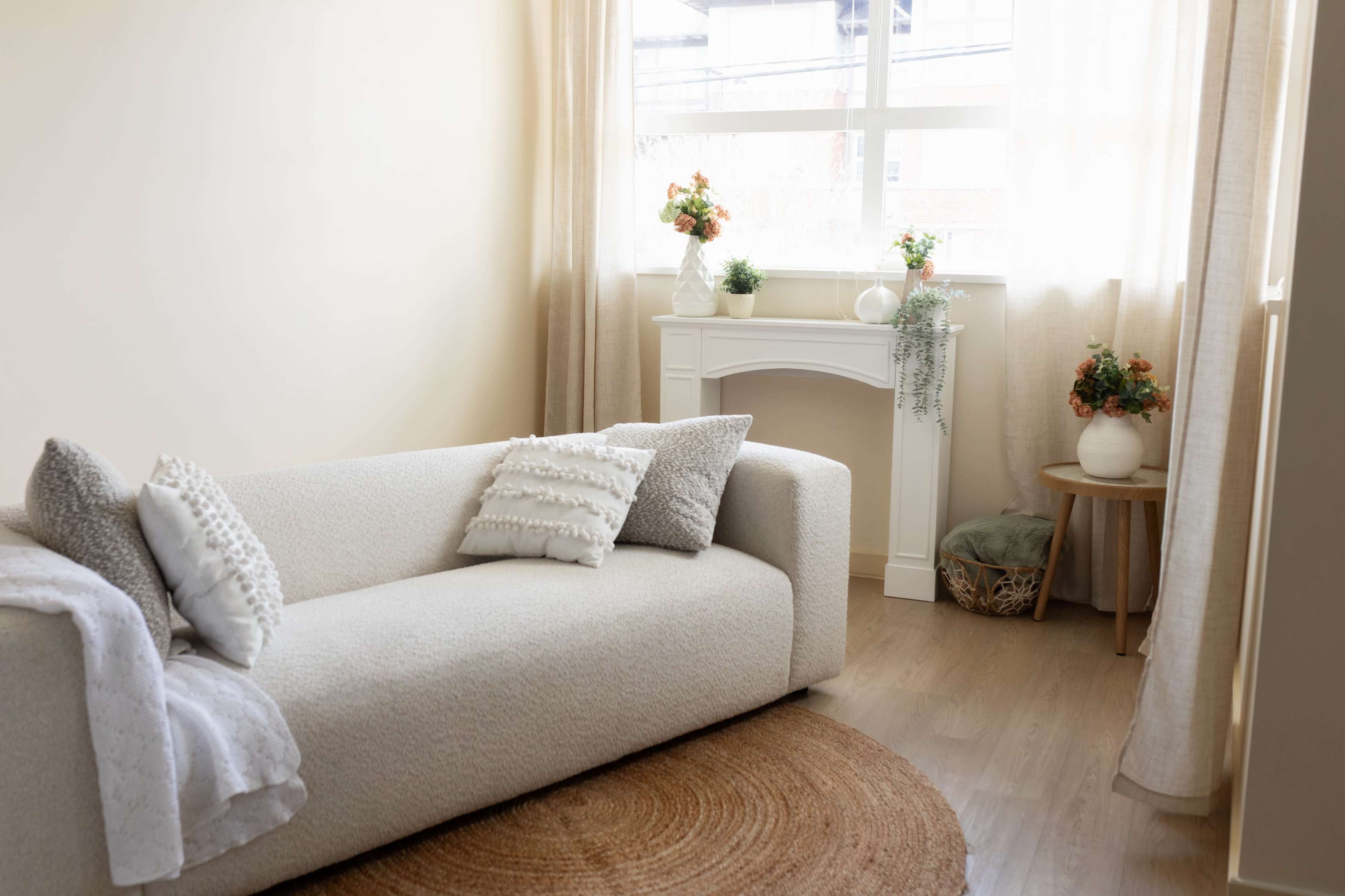 A light-colored living room features a modern sofa, a round rug, and a small table adorned with potted plants and decorative items.