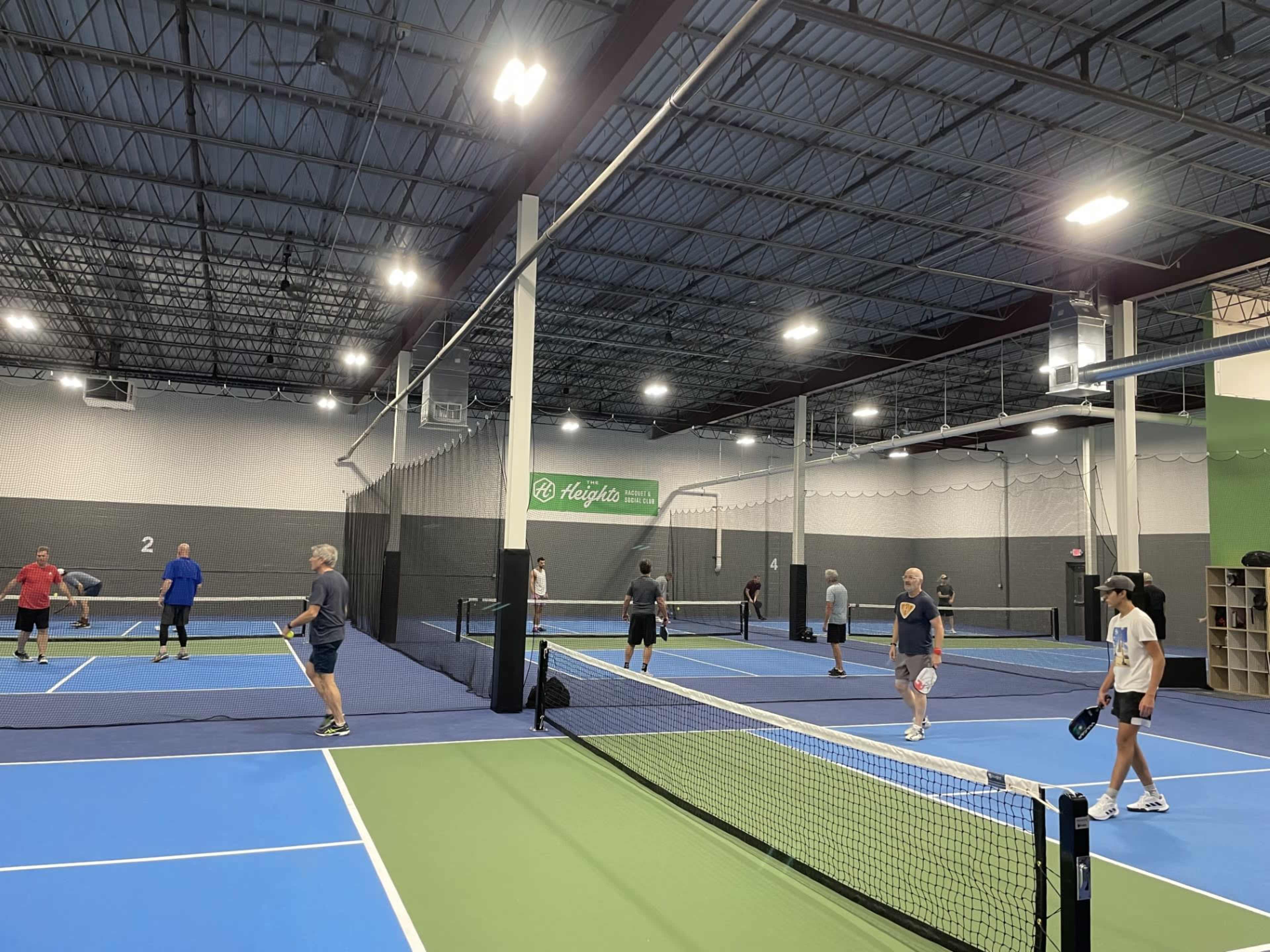 A group of players is engaged in various matches on several indoor tennis courts.
