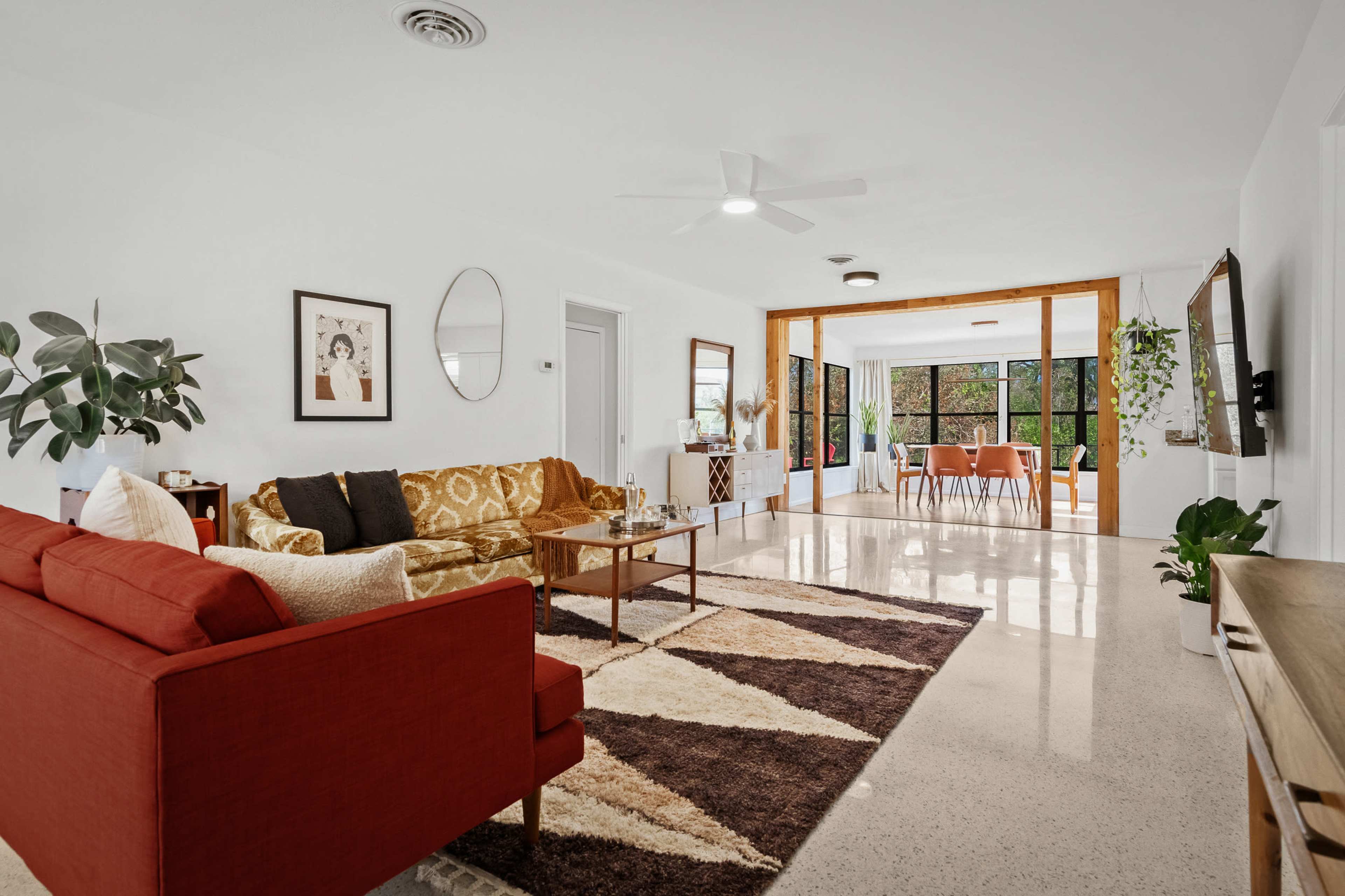 The living room features two sofas, a coffee table, and a large window leading to a dining area with a table and chairs.