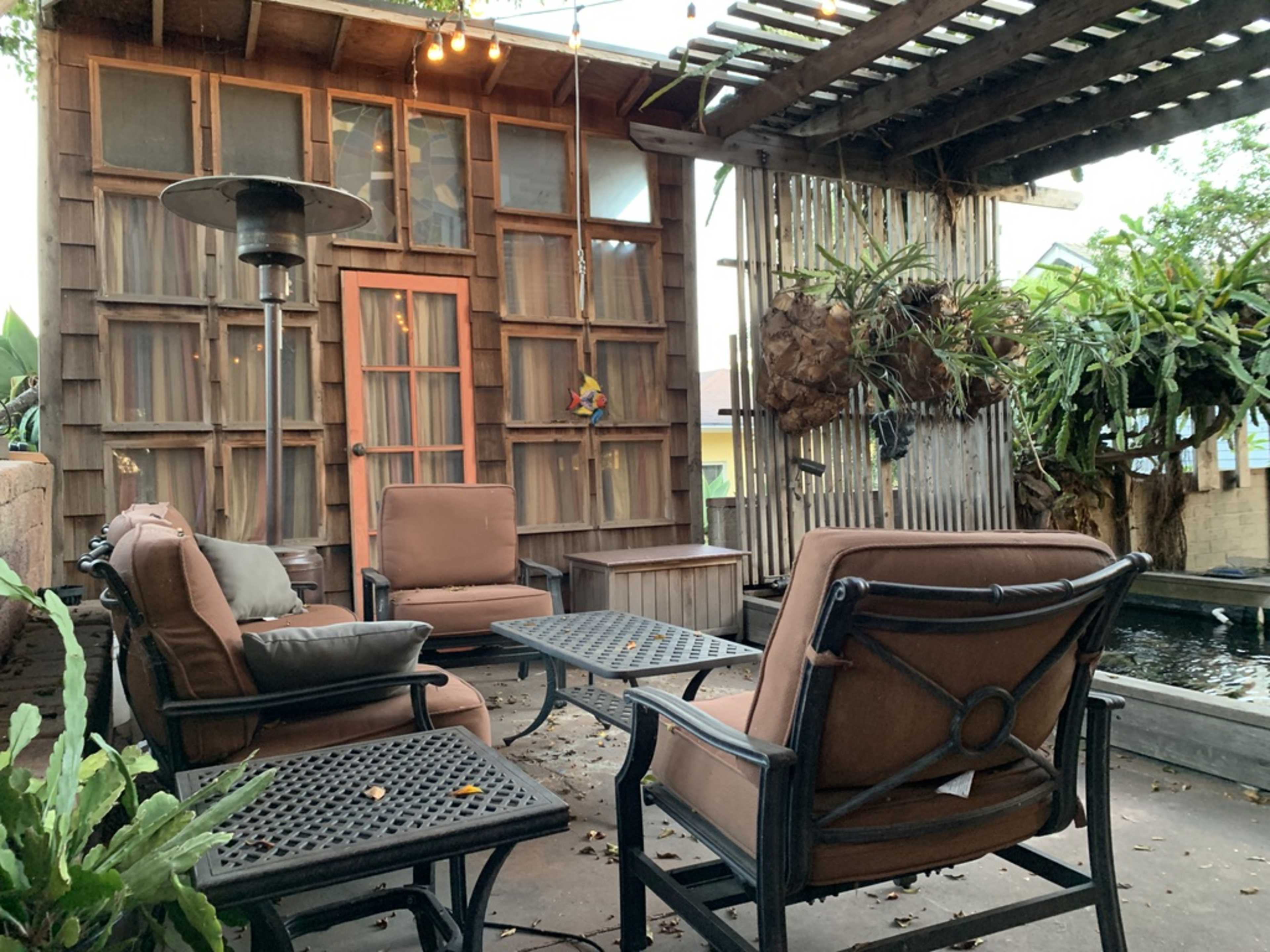 A cozy outdoor seating area features brown metal-framed chairs and a table, surrounded by a wooden structure and greenery.