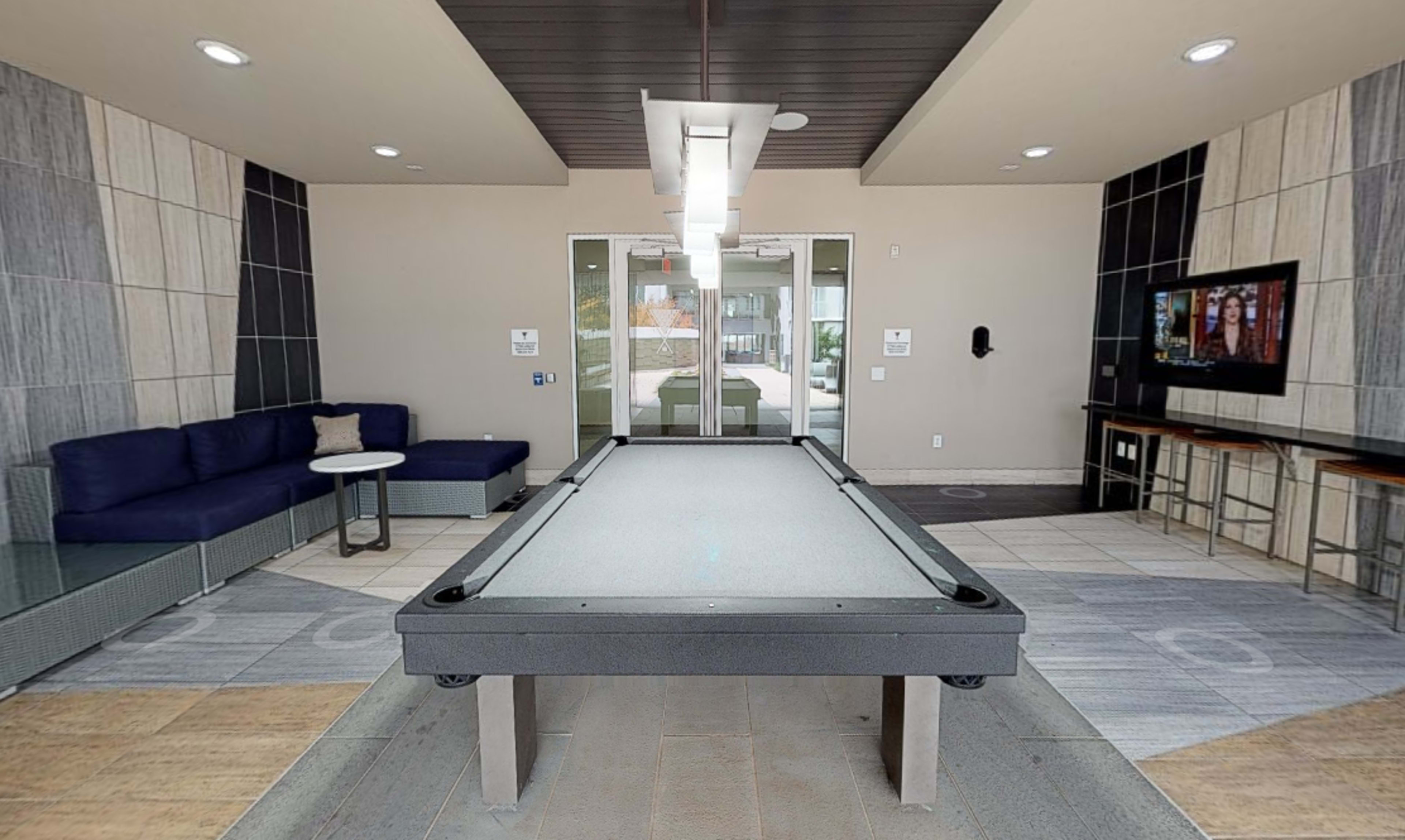 A modern lounge area featuring a pool table, a sofa, a small table, and a wall-mounted television.