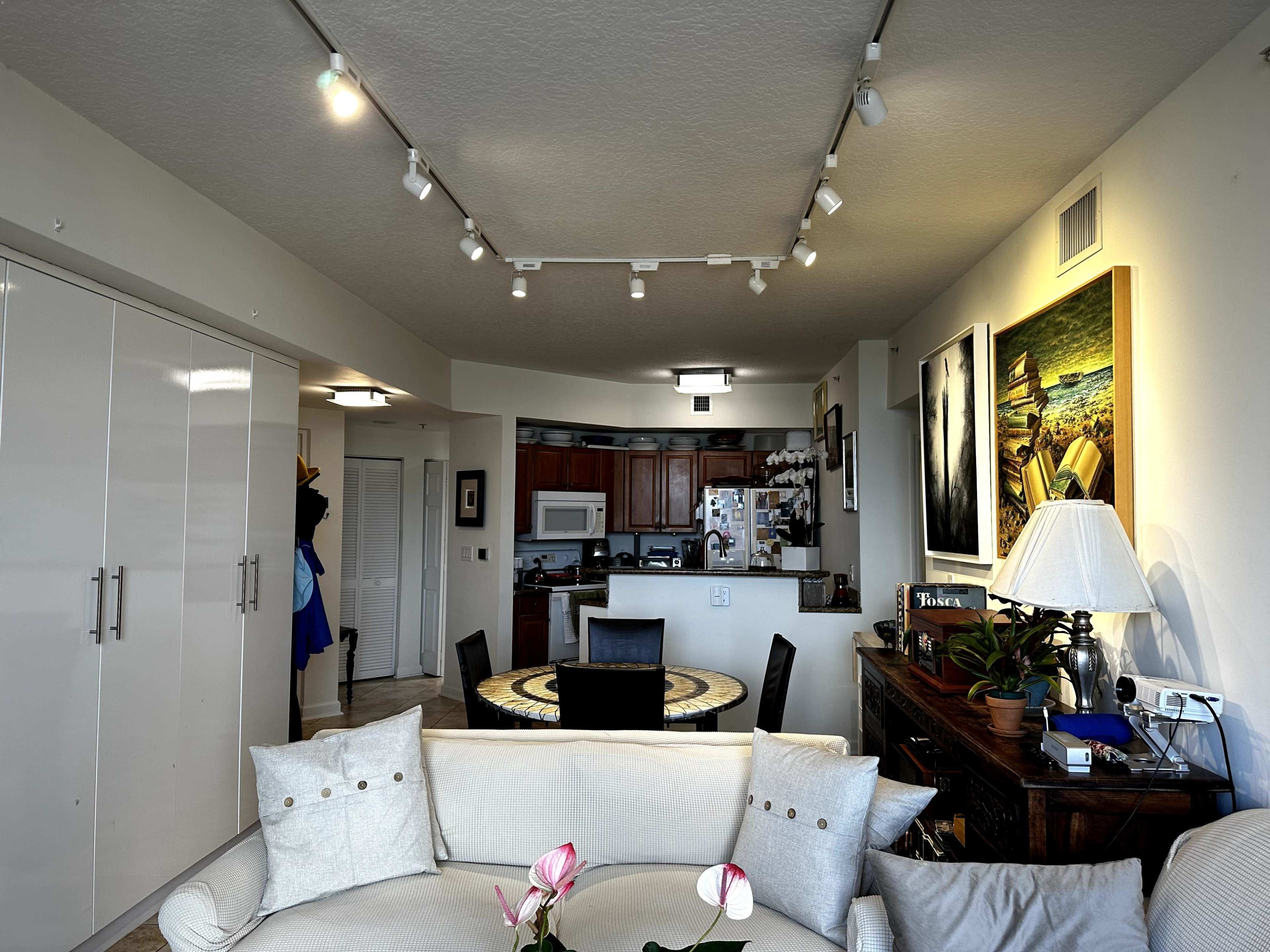A living room area with a sectional sofa, a round table, and a kitchen visible in the background.
