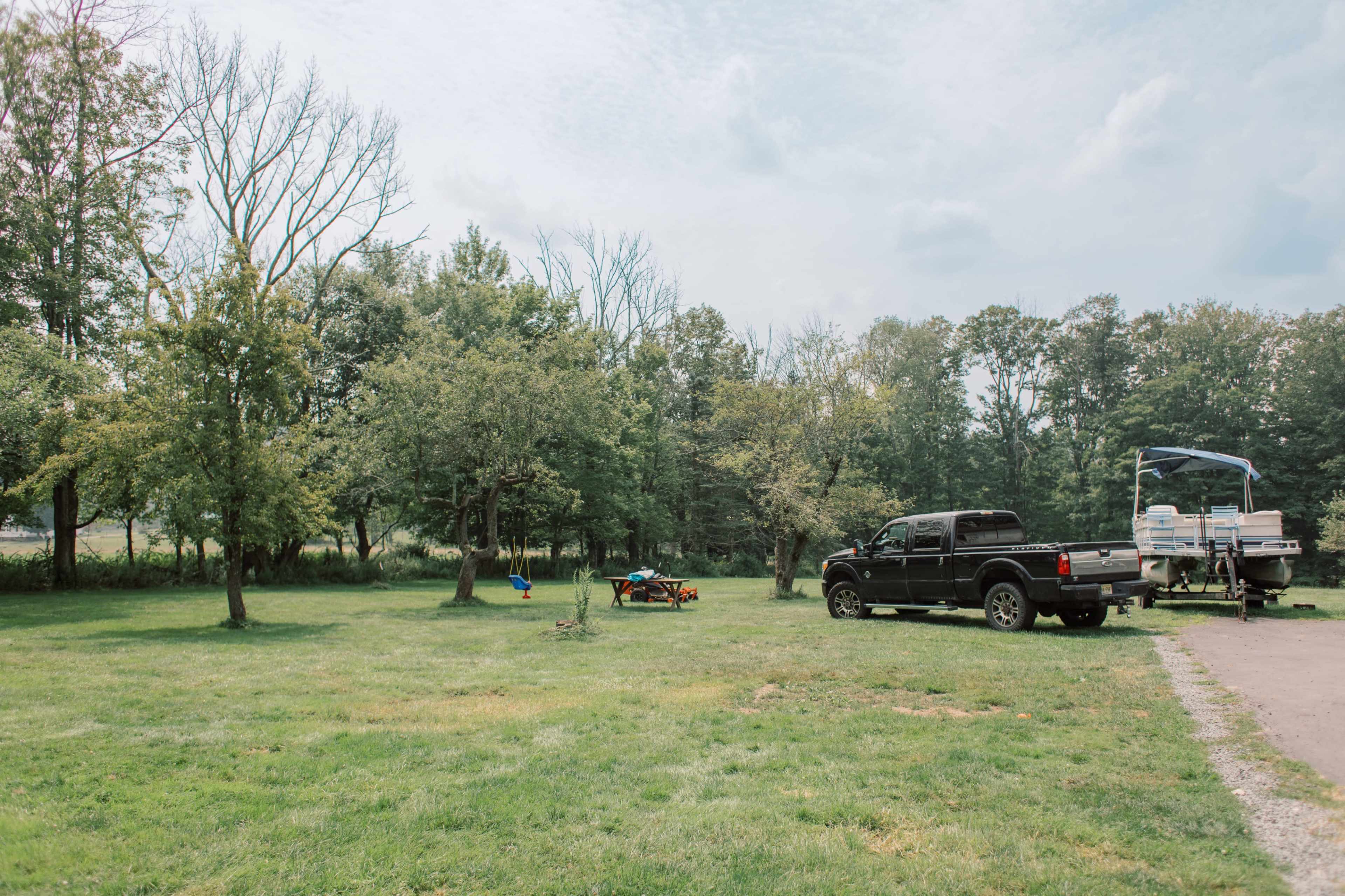 A black pickup truck is parked on a grassy area next to trees and a small trailer.