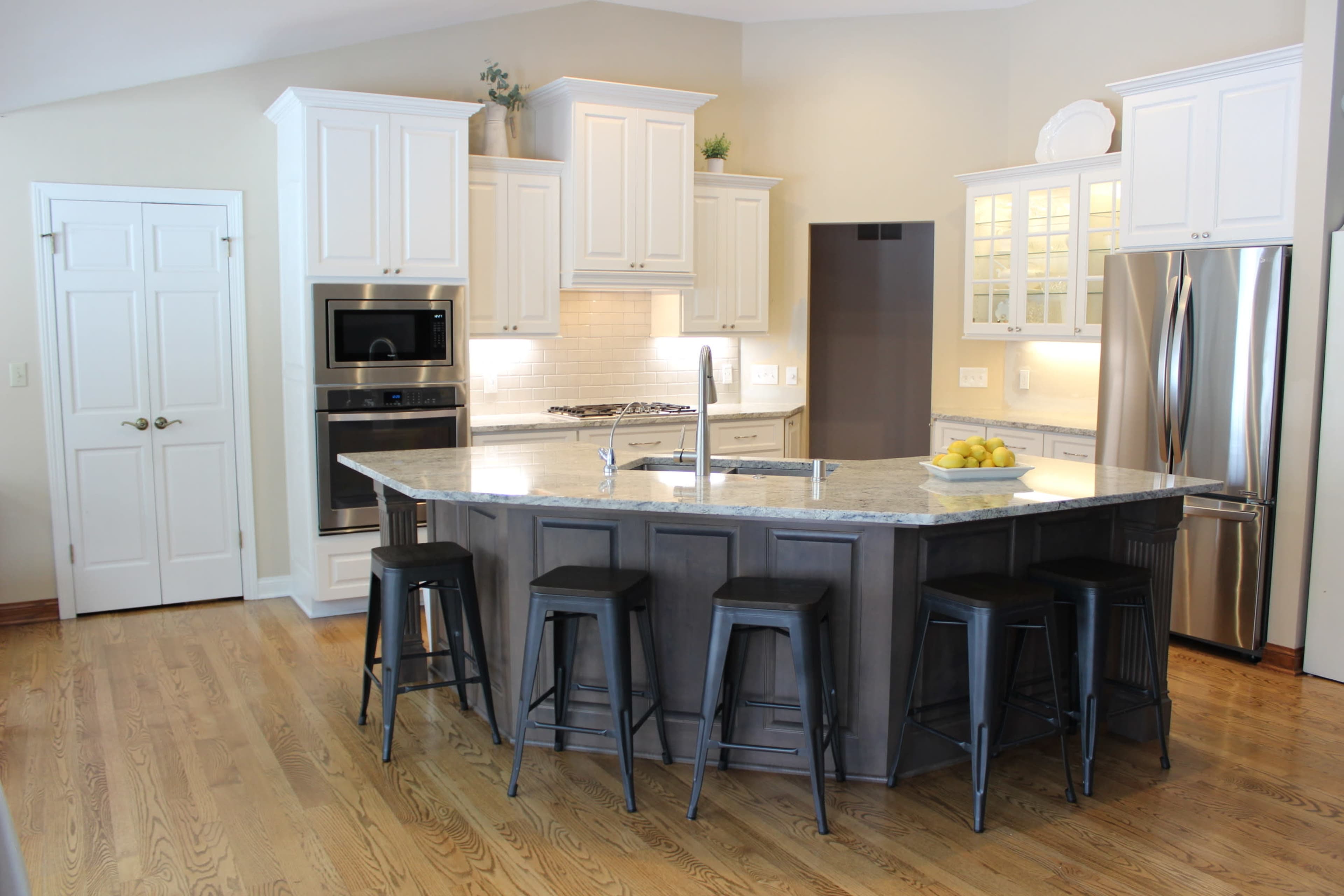 A modern kitchen with white cabinets, a central island with bar stools, and stainless steel appliances.