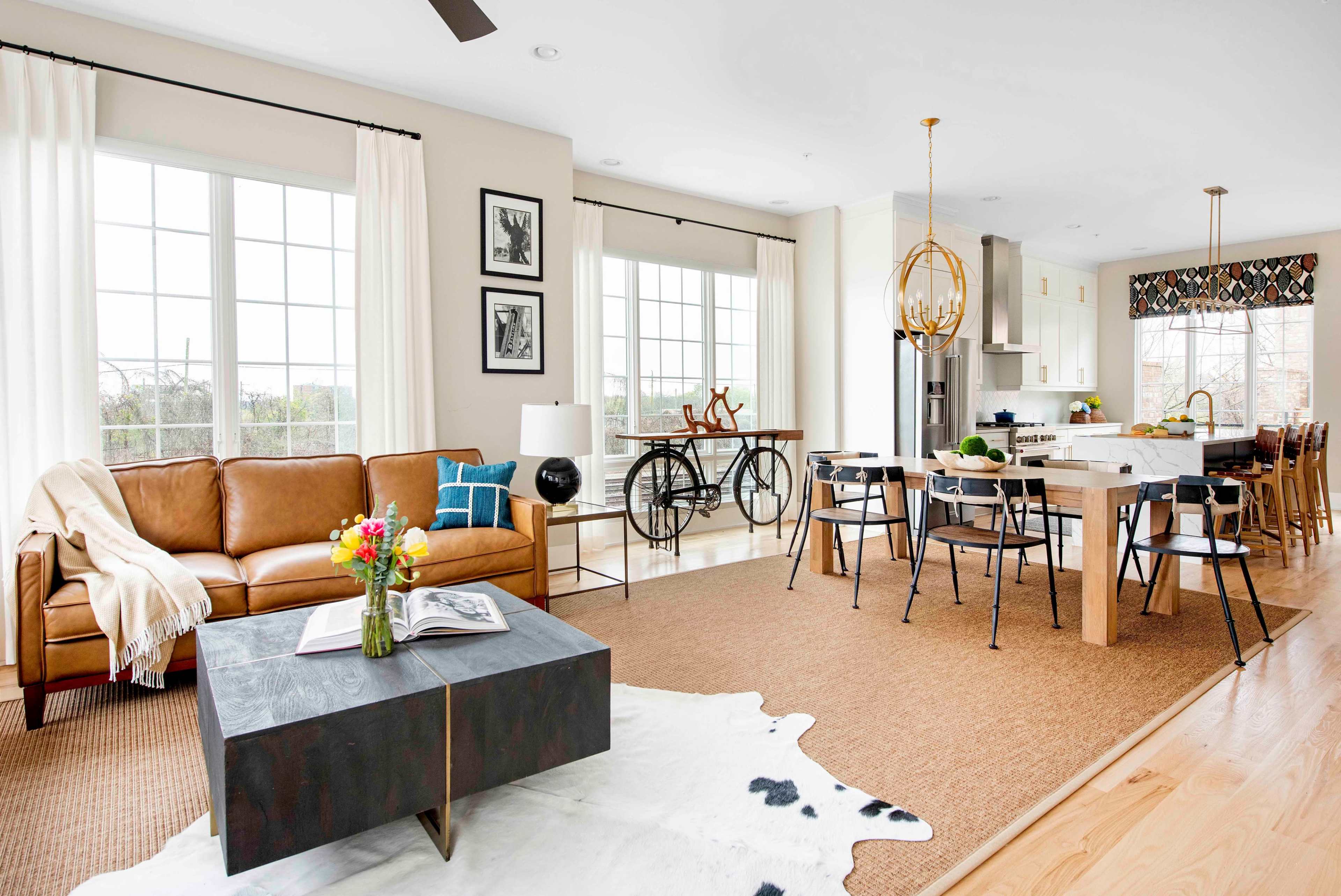 The image shows a modern open-concept living and dining area with a brown leather sofa, a black coffee table, and a large dining table surrounded by black chairs.