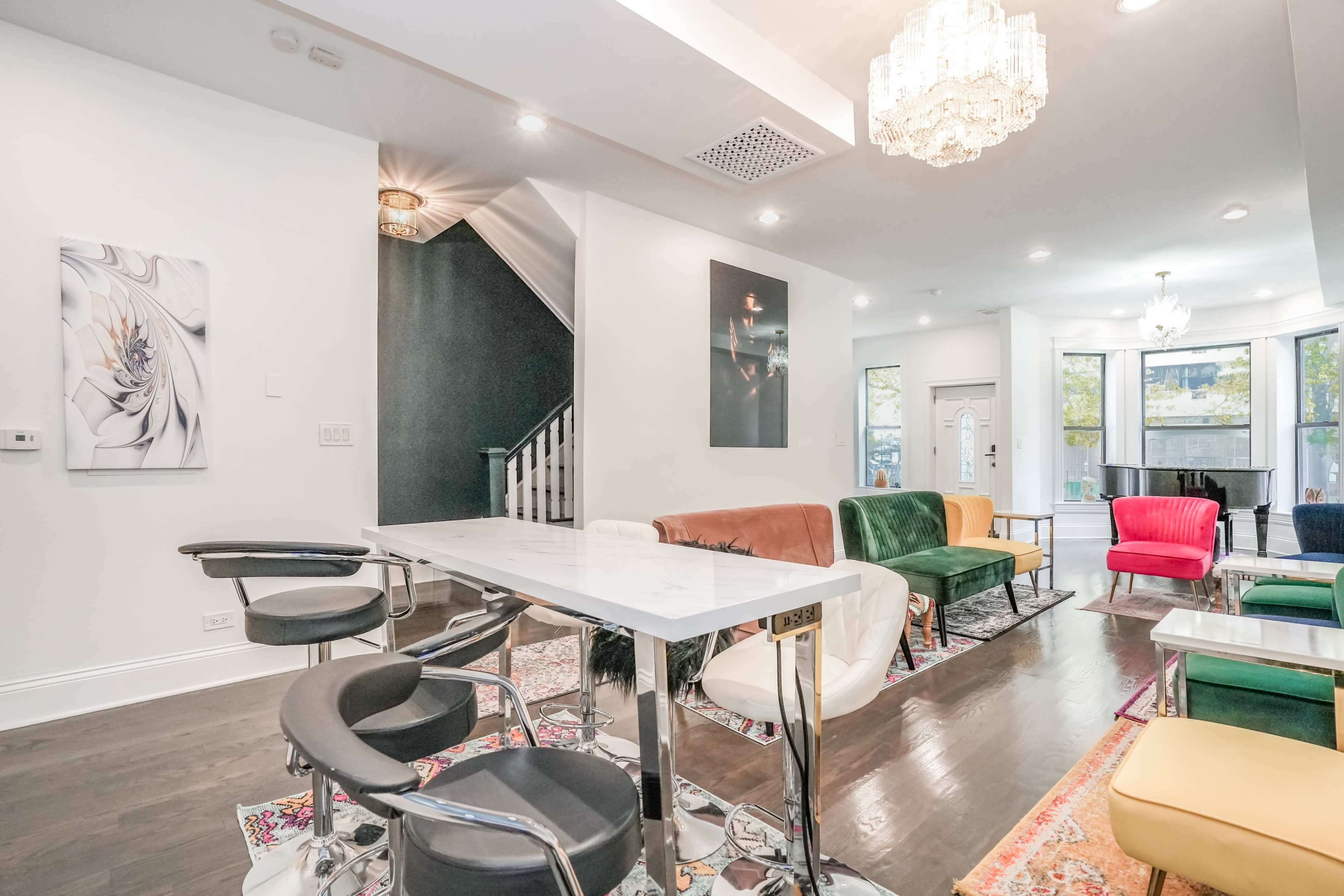 A modern living space featuring a dining table with high chairs, colorful sofas, and a staircase in the background.