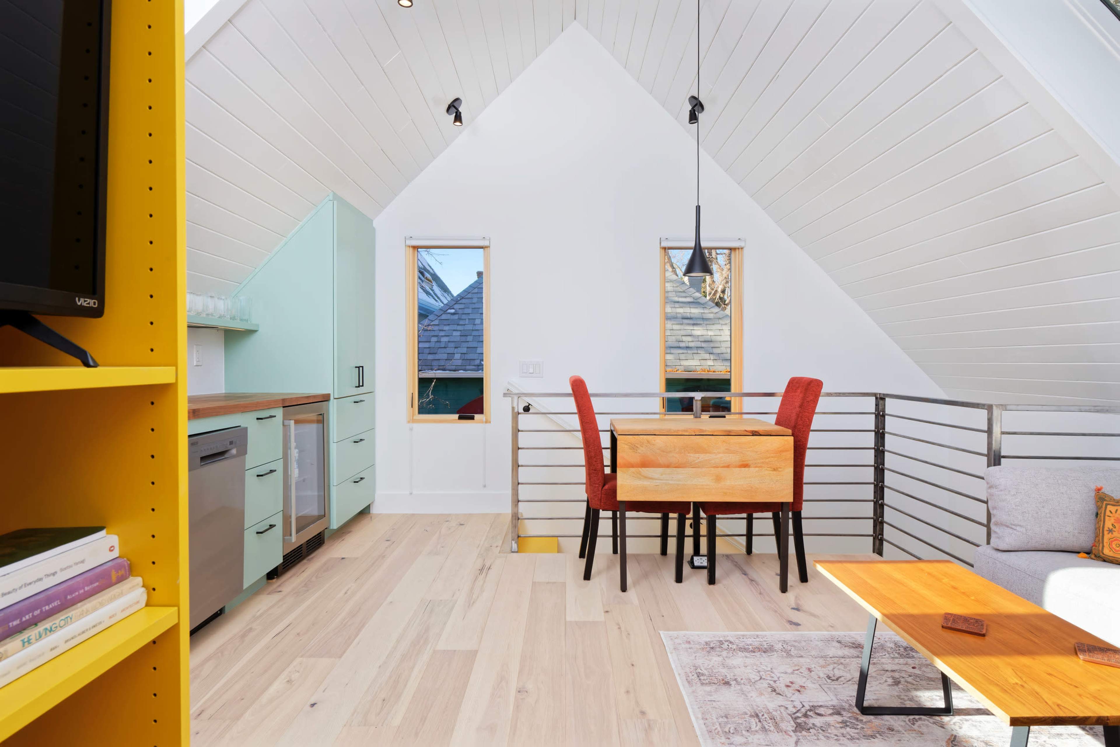 The image shows a compact kitchen and dining area in a modern, brightly lit room with high ceilings and wood flooring.