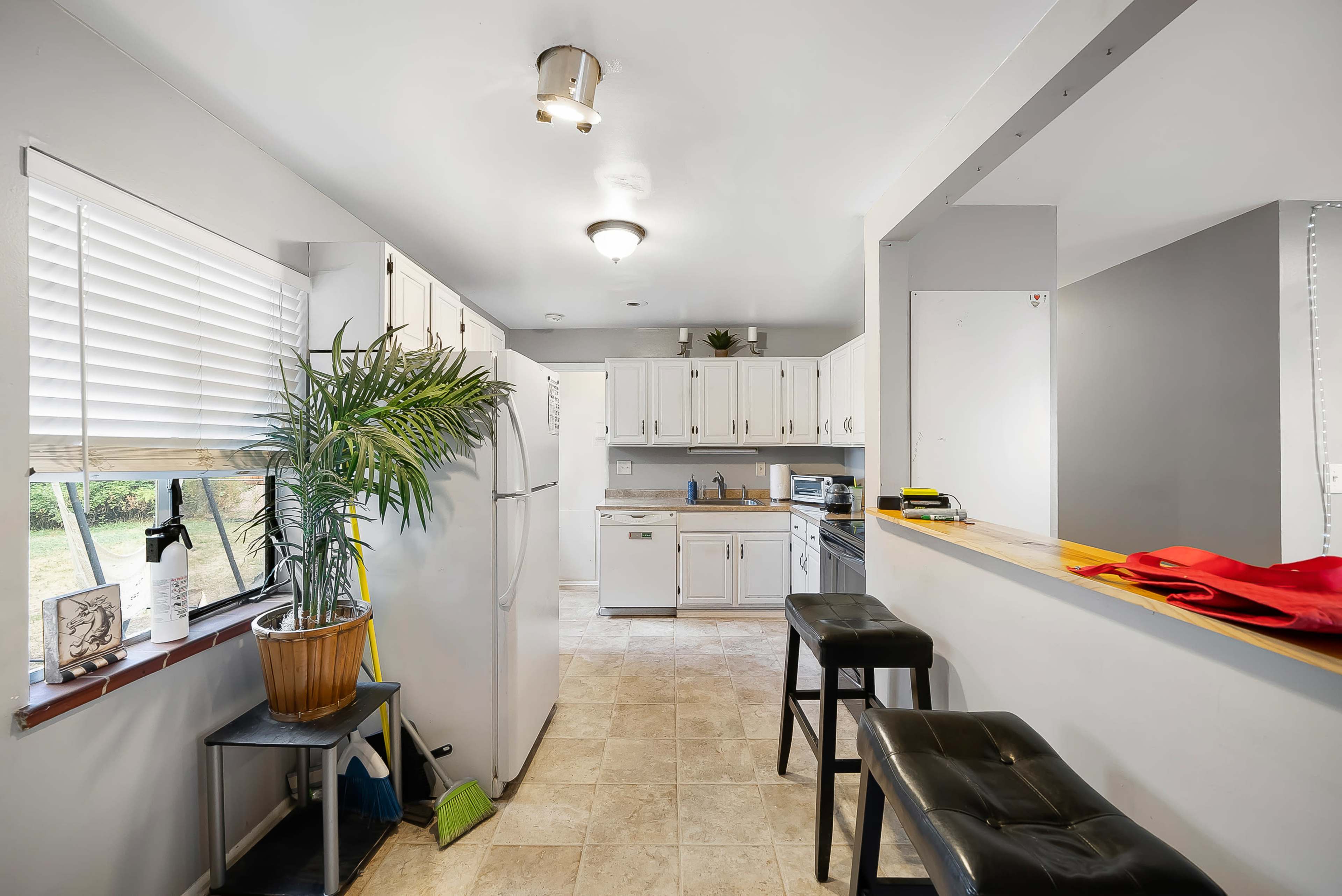 A modern kitchen features white cabinetry, a refrigerator, and a bar area with stools, alongside a window that lets in natural light.