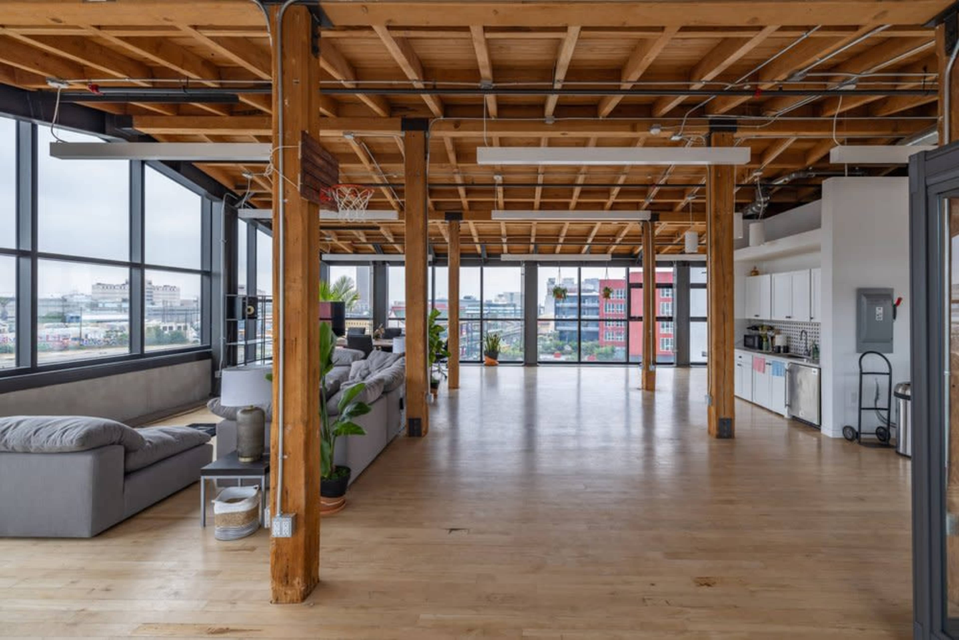 A spacious, open-concept loft with wooden beams, large windows, and a minimalist kitchen area.