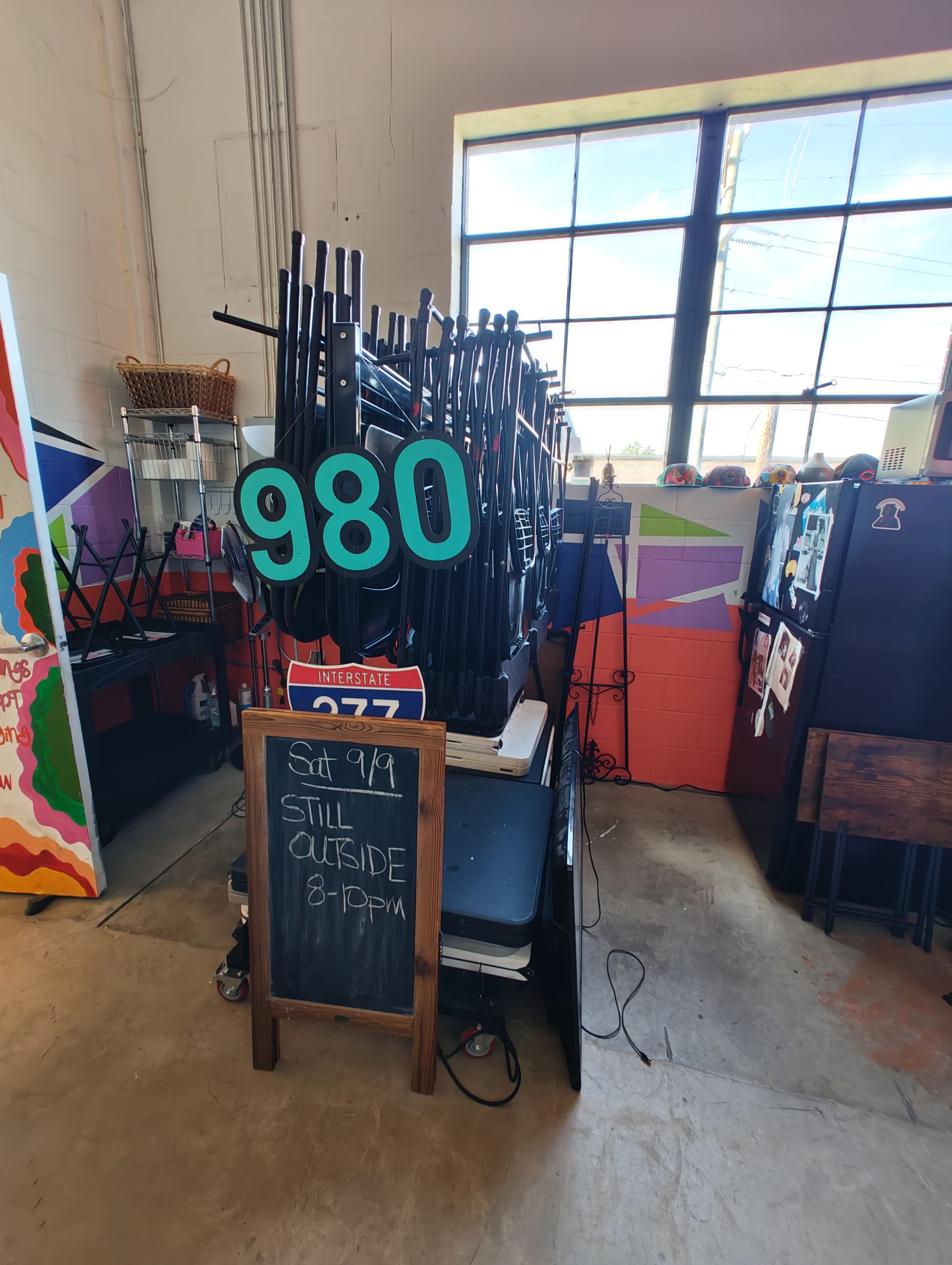 A stack of black chairs and tables is displayed next to a chalkboard sign indicating an event on Saturday, September 9, from 8 to 10 PM.